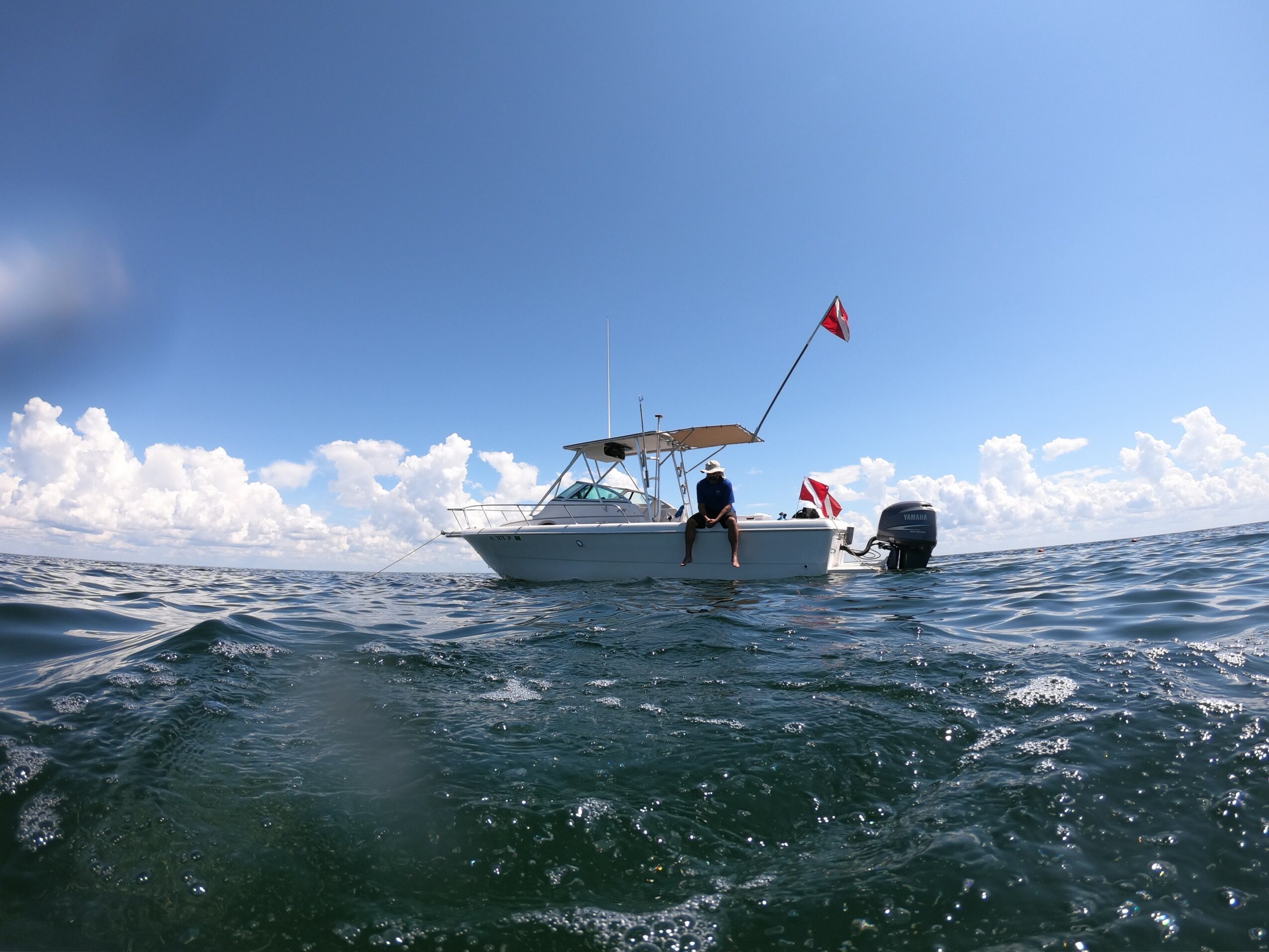 Boat with a person on the water under a blue sky with clouds, viewed from the water surface.