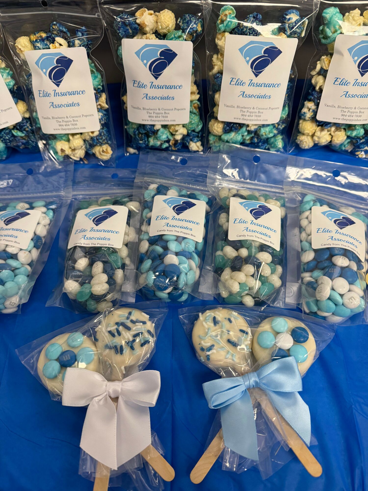 Multiple clear bags of blue and white candies and two decorated lollipops with bows, on a blue surface.