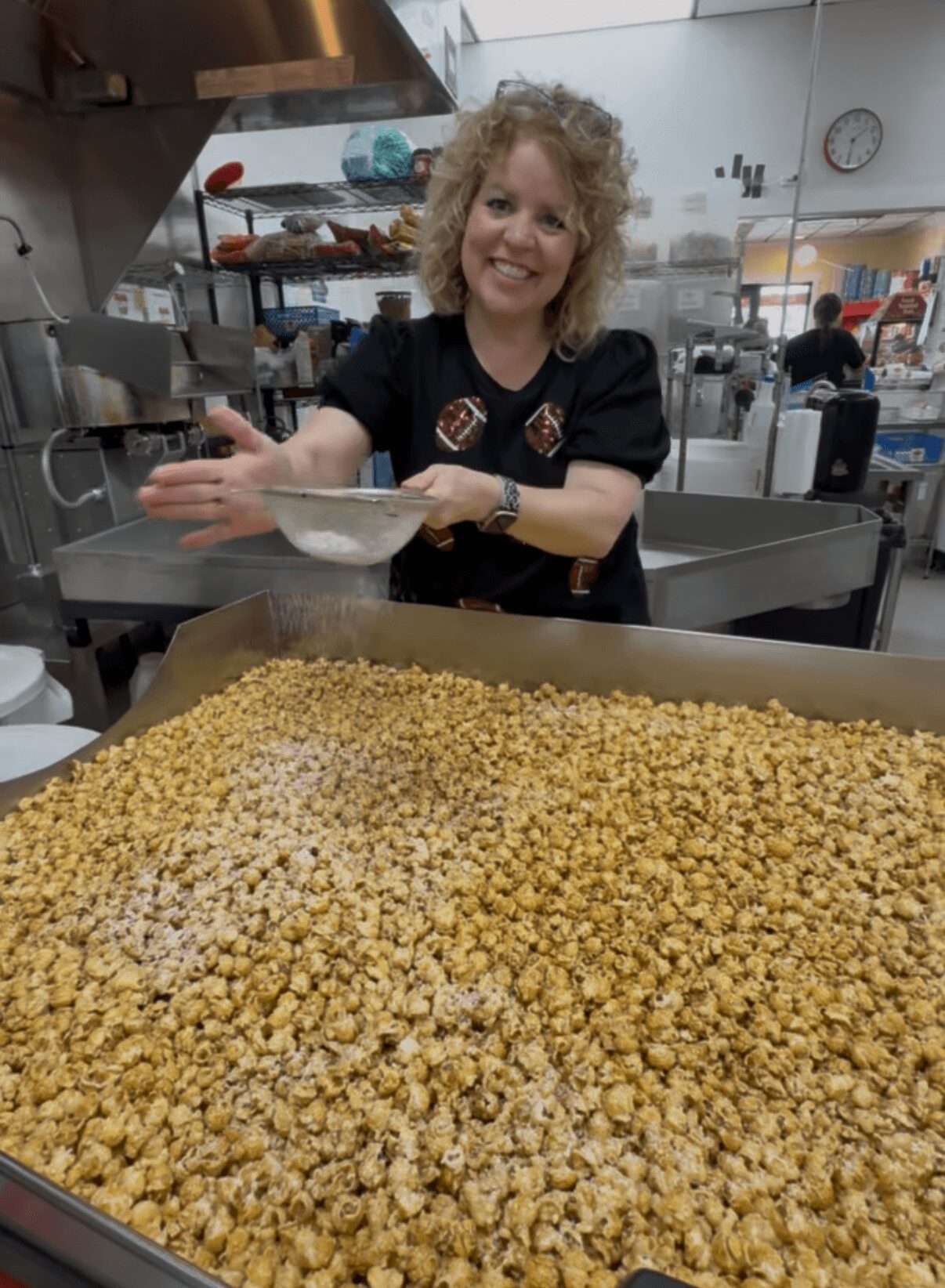 Woman smiling and holding a bowl in a kitchen with a large tray of popcorn in front.