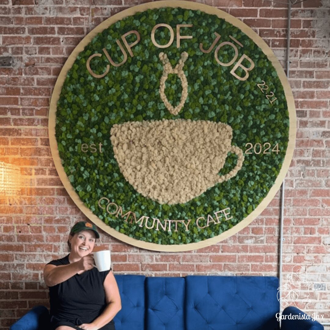 Large circular sign with a green background and a white coffee cup, surrounded by brick wall, with a woman holding a mug below.