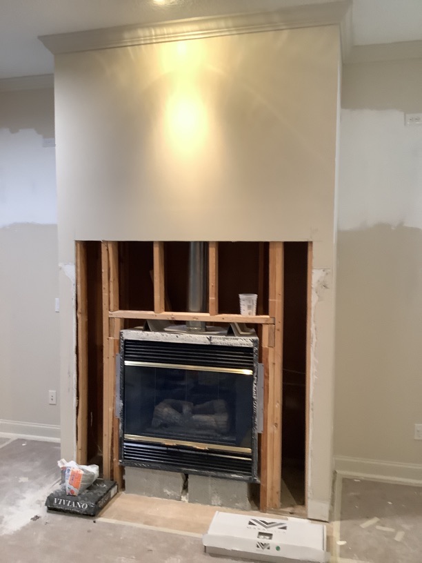 Fireplace with exposed wooden framing and a black insert, surrounded by unfinished wall and construction materials on the floor.