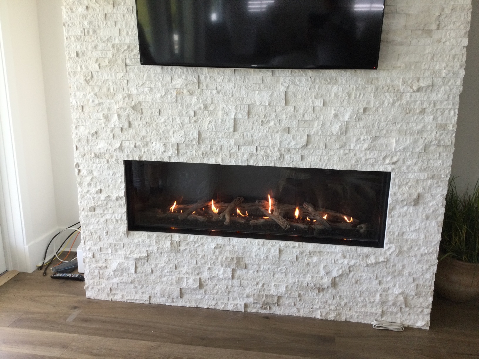 White textured wall with a mounted flat-screen TV above a modern rectangular fireplace with visible flames.