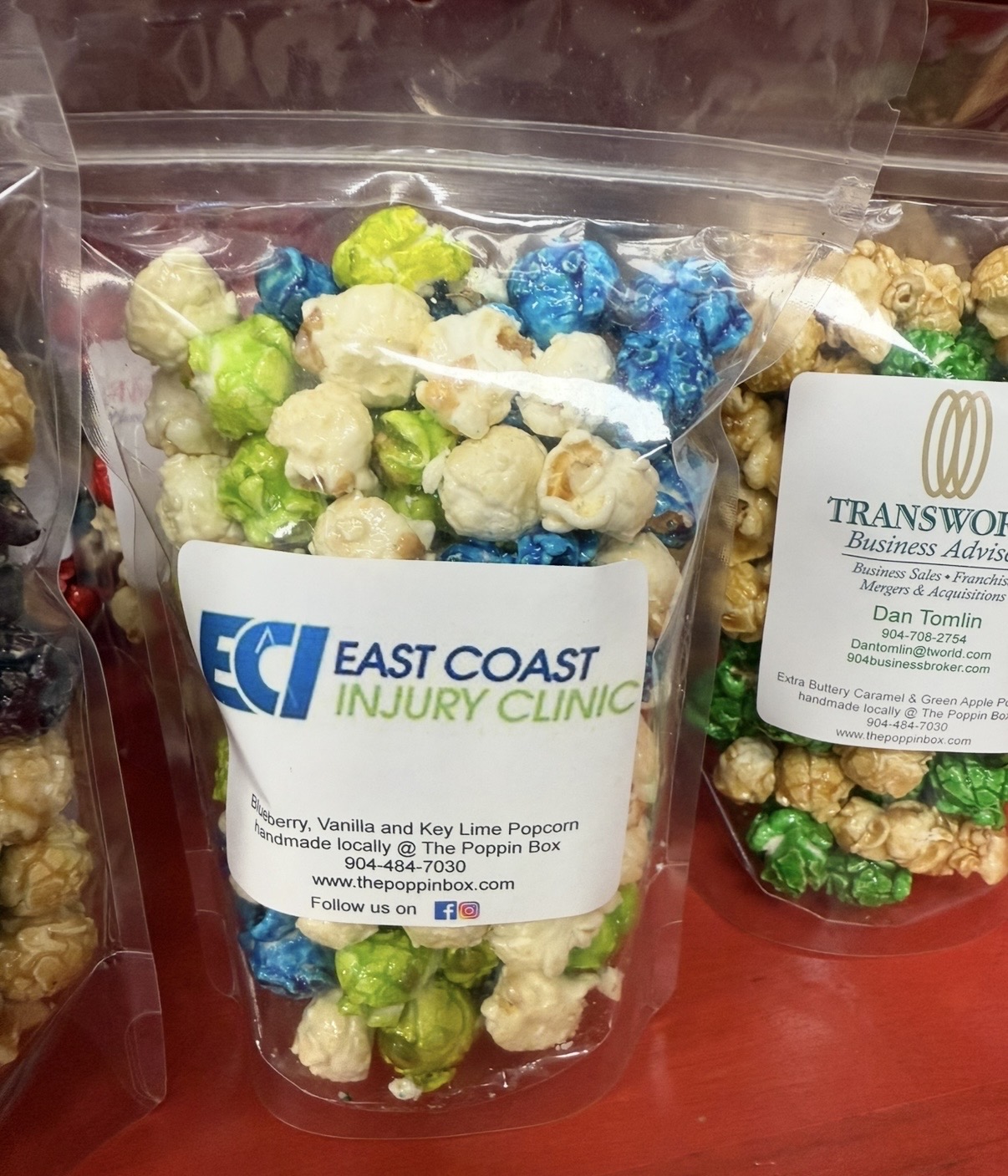 Clear plastic bag filled with colorful popcorn in green, blue, and white, on a red surface.