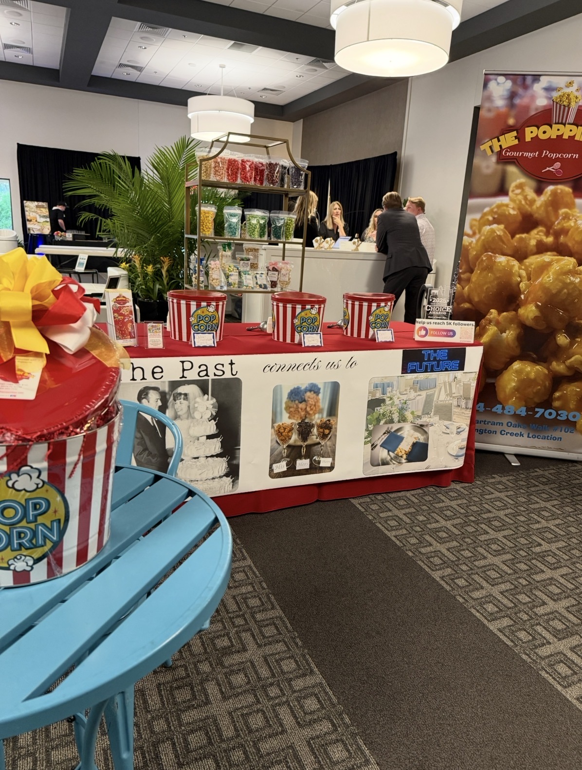 Popcorn stand with red chairs, posters, and a large popcorn poster in the background, inside a decorated room.