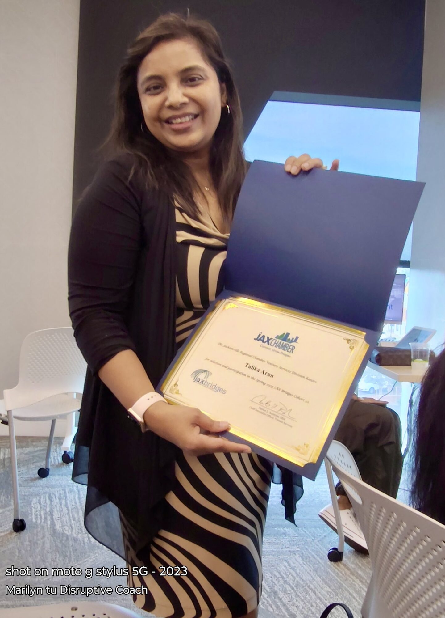 Woman holding a certificate in a room with chairs and a window behind her.