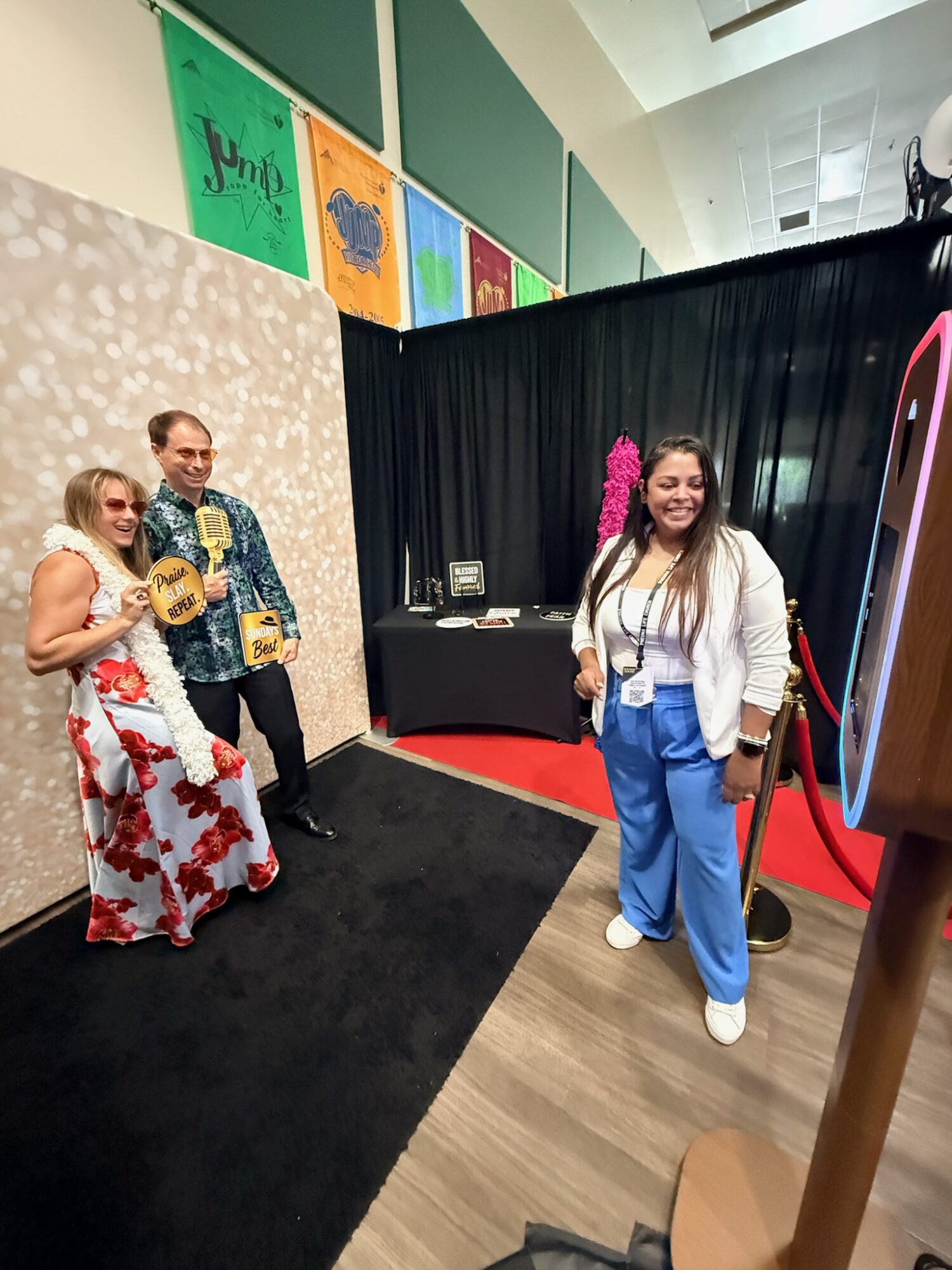 Three people posing for a photo in front of a black curtain, with colorful artwork on the wall behind them.