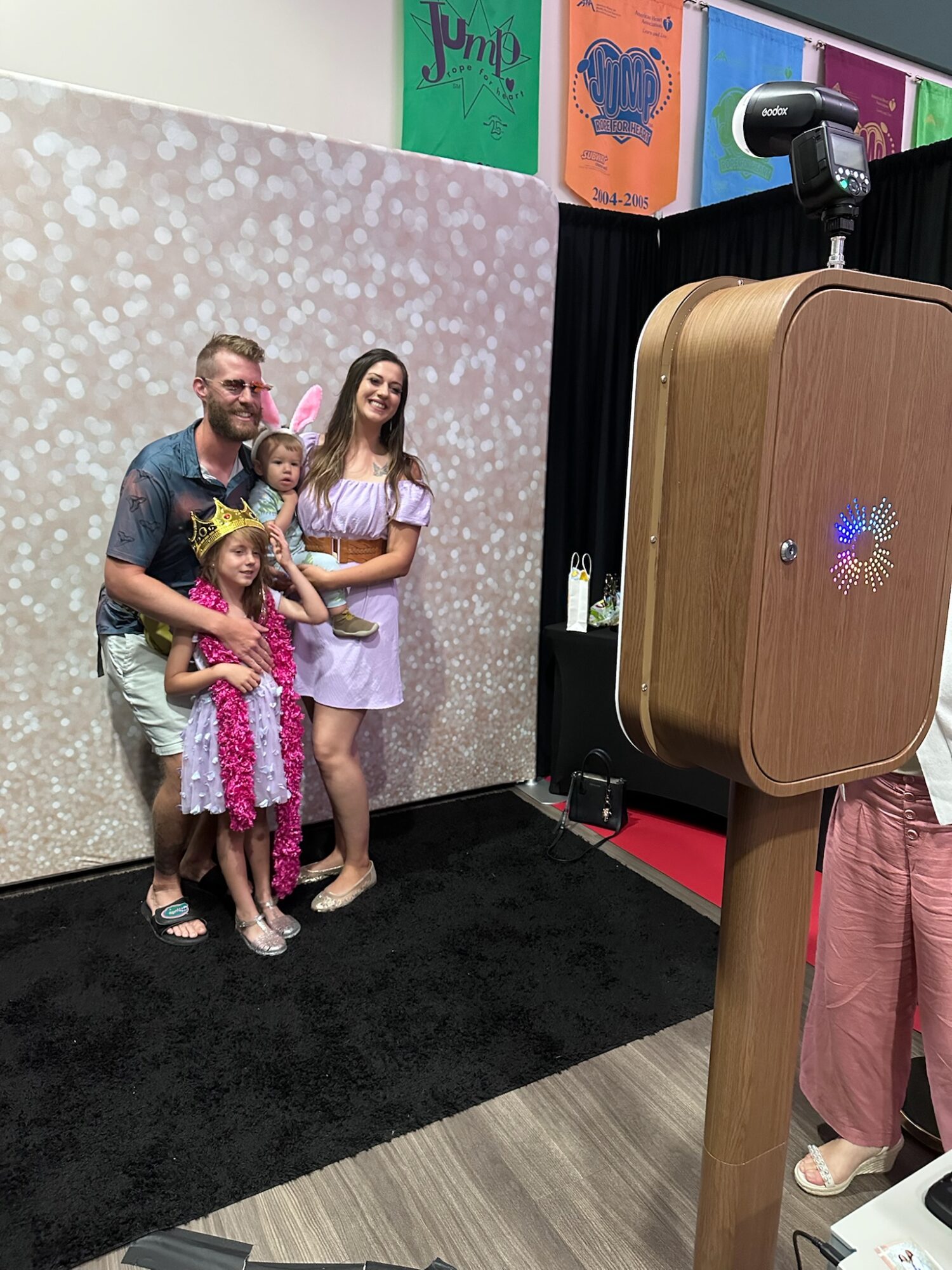 Group of four people, two adults and two children, posing for a photo in front of a decorated backdrop.