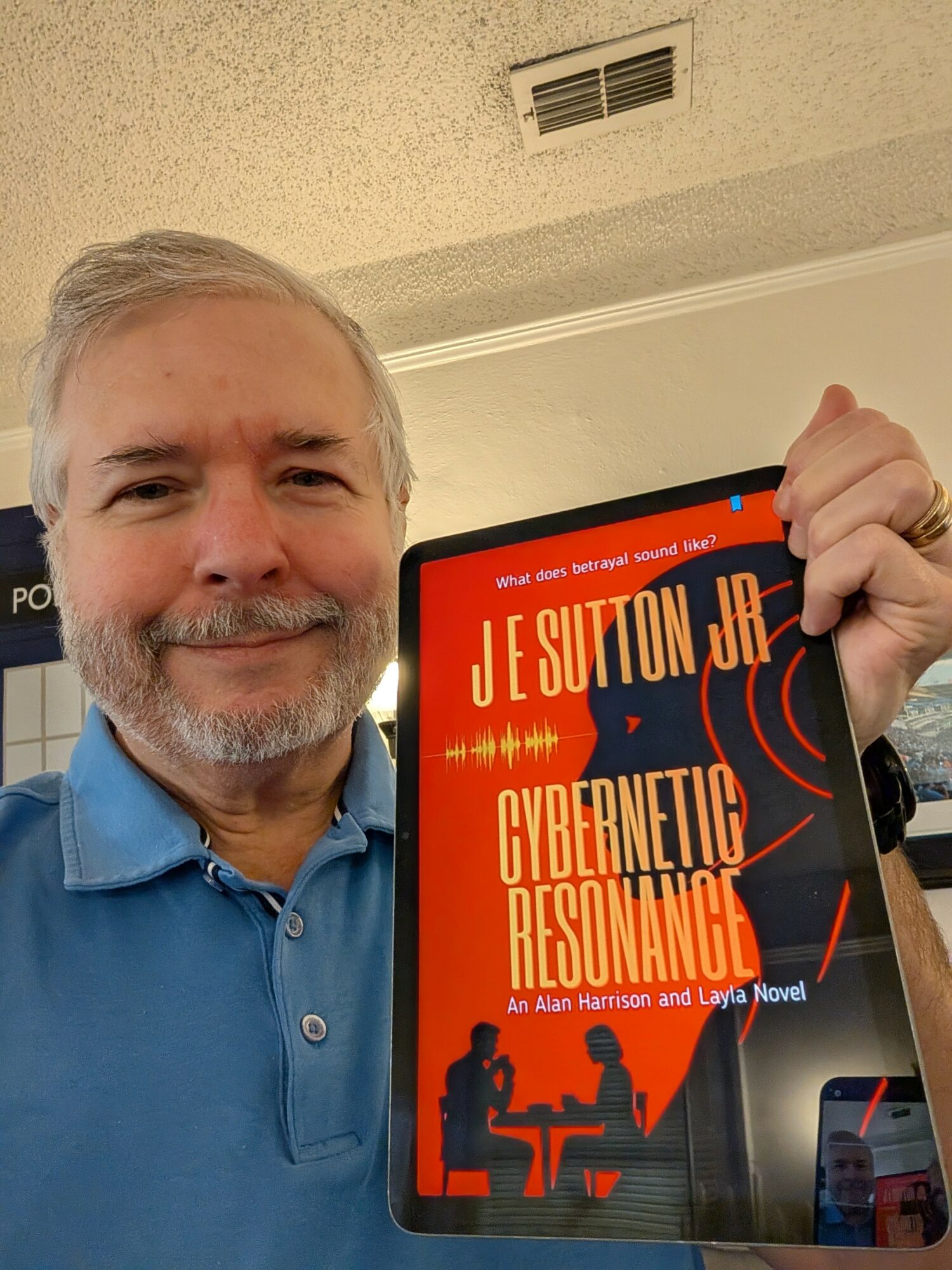Man with gray hair and beard smiling, holding a book titled 'Cybernetic Resonance' in front of a wall with a vent.