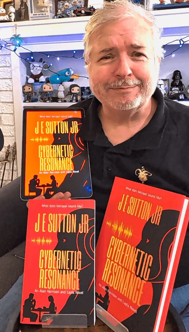 Man with gray hair and beard holding three copies of a book titled 'Cybernetic Resonance' in front of a display with toys.