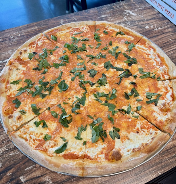 Cheese pizza topped with chopped green herbs on a glass plate, on a wooden table.