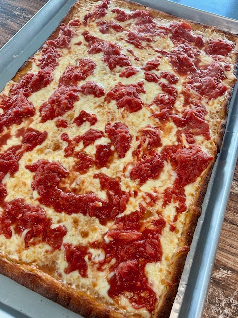 Rectangular pizza with cheese and tomato topping on a baking tray.