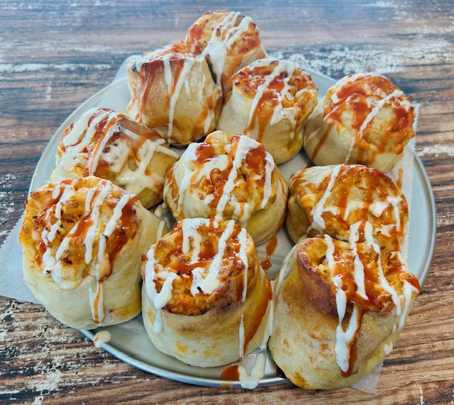 Plate of cinnamon rolls drizzled with icing on a wooden table.