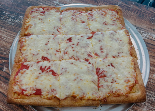 Rectangular cheese pizza with nine slices on a round tray, cheese melted and slightly browned.