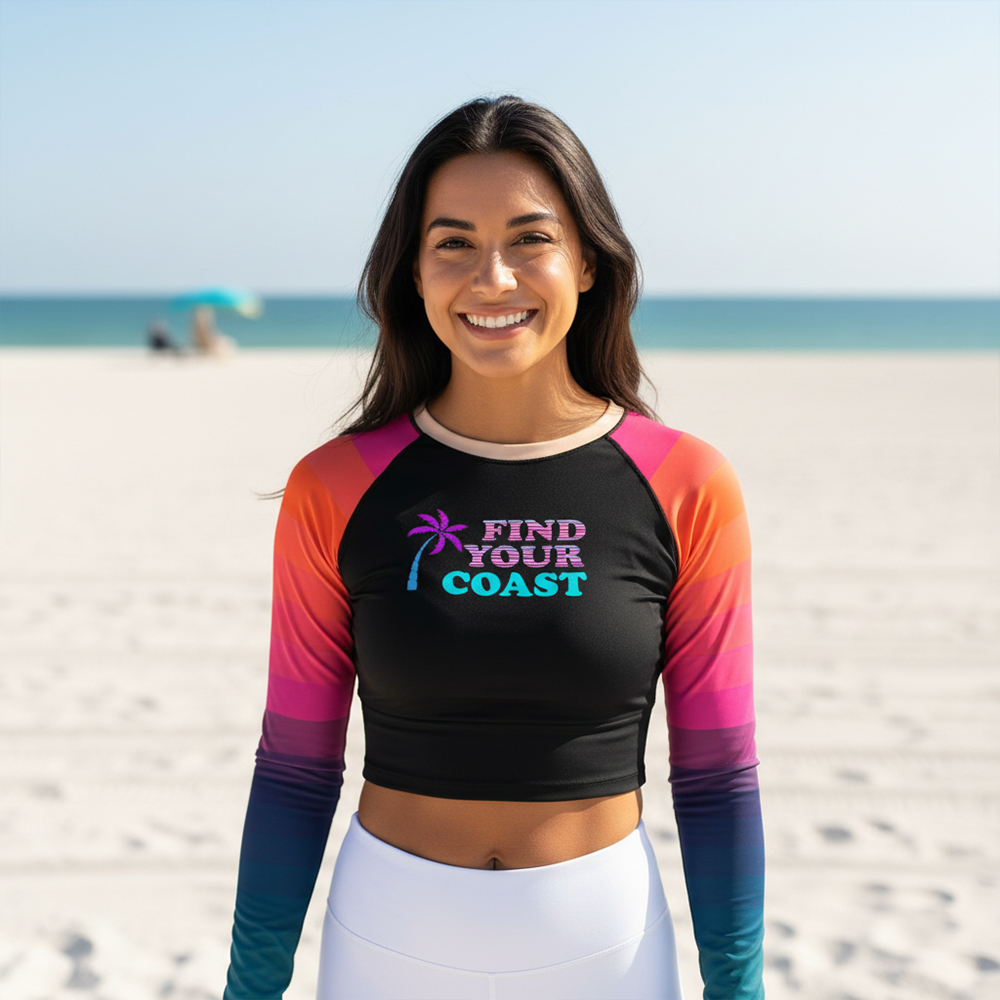 Smiling woman in colorful long-sleeve top at the beach with sand and ocean in background.