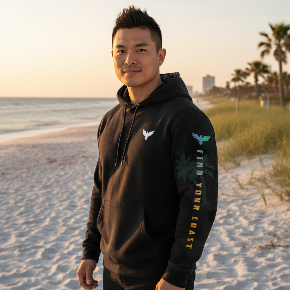 Young man standing on a beach with sand, ocean, and palm trees in the background during sunset.