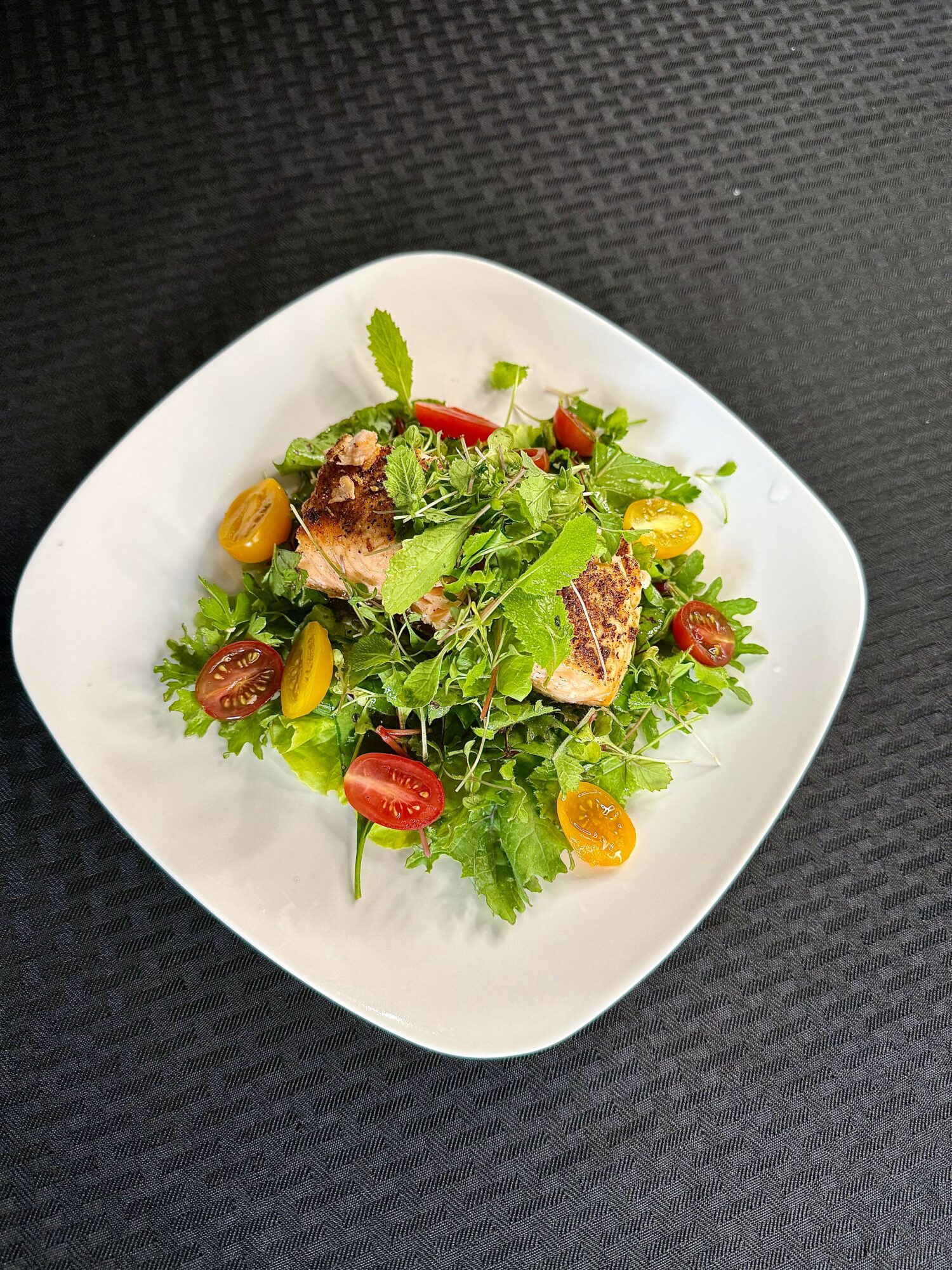 Fresh salad with mixed greens, cherry tomatoes, and grilled chicken pieces on a white plate.