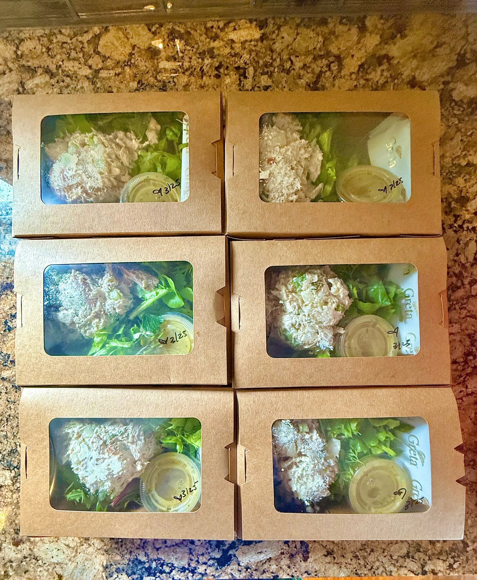 Six boxes with transparent windows showing flowers and small jars inside, arranged in two rows of three on a surface.