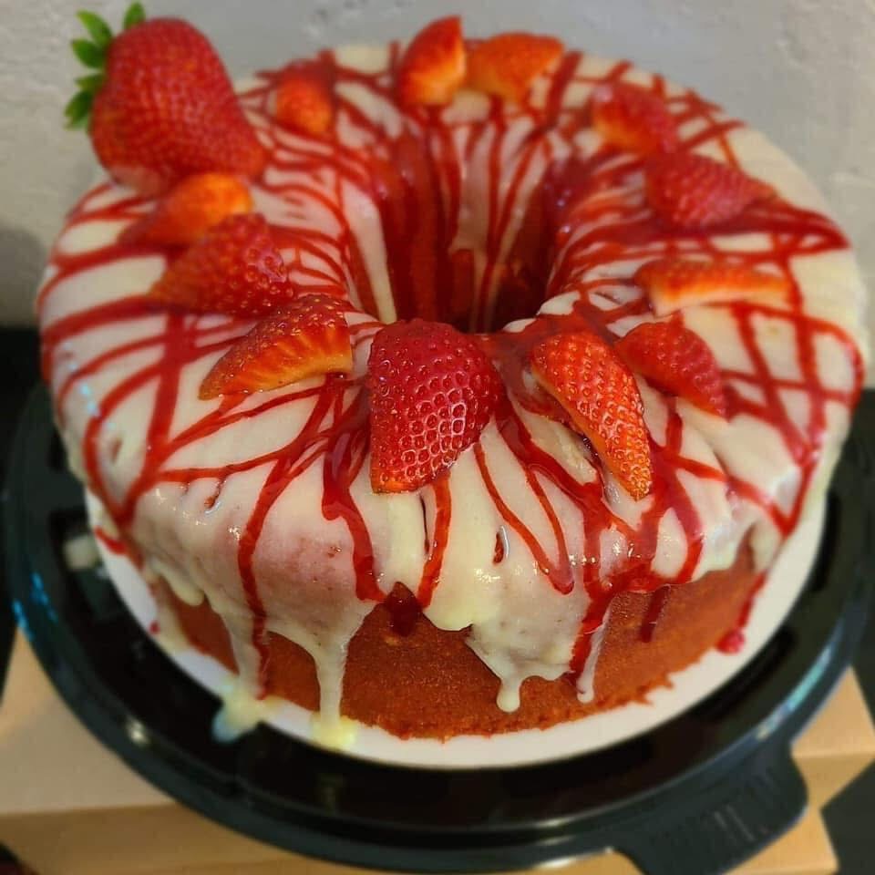 Cake with white frosting, strawberries, and red drizzle on top, on a black plate.