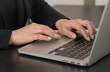 Person typing on a laptop keyboard with hands visible, on a dark surface.
