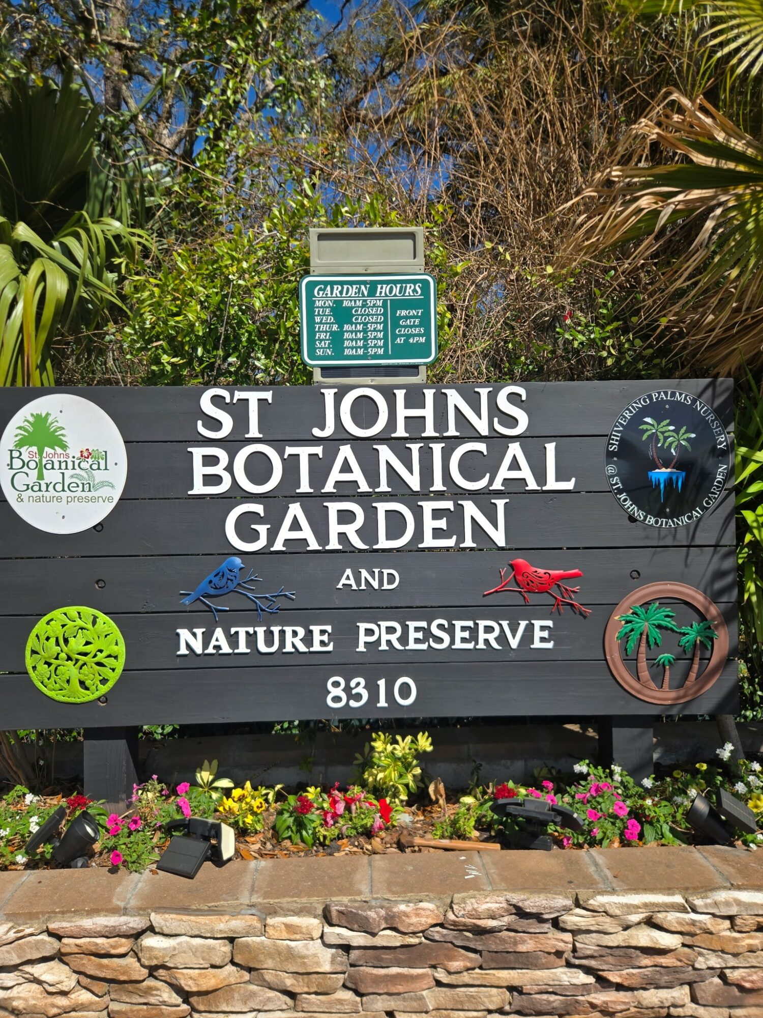 Sign for St. Johns Botanical Garden and Nature Preserve with colorful decorations and plants at the base.