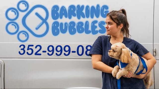 Woman holding a dog in front of a van with a logo and phone number for a pet service.