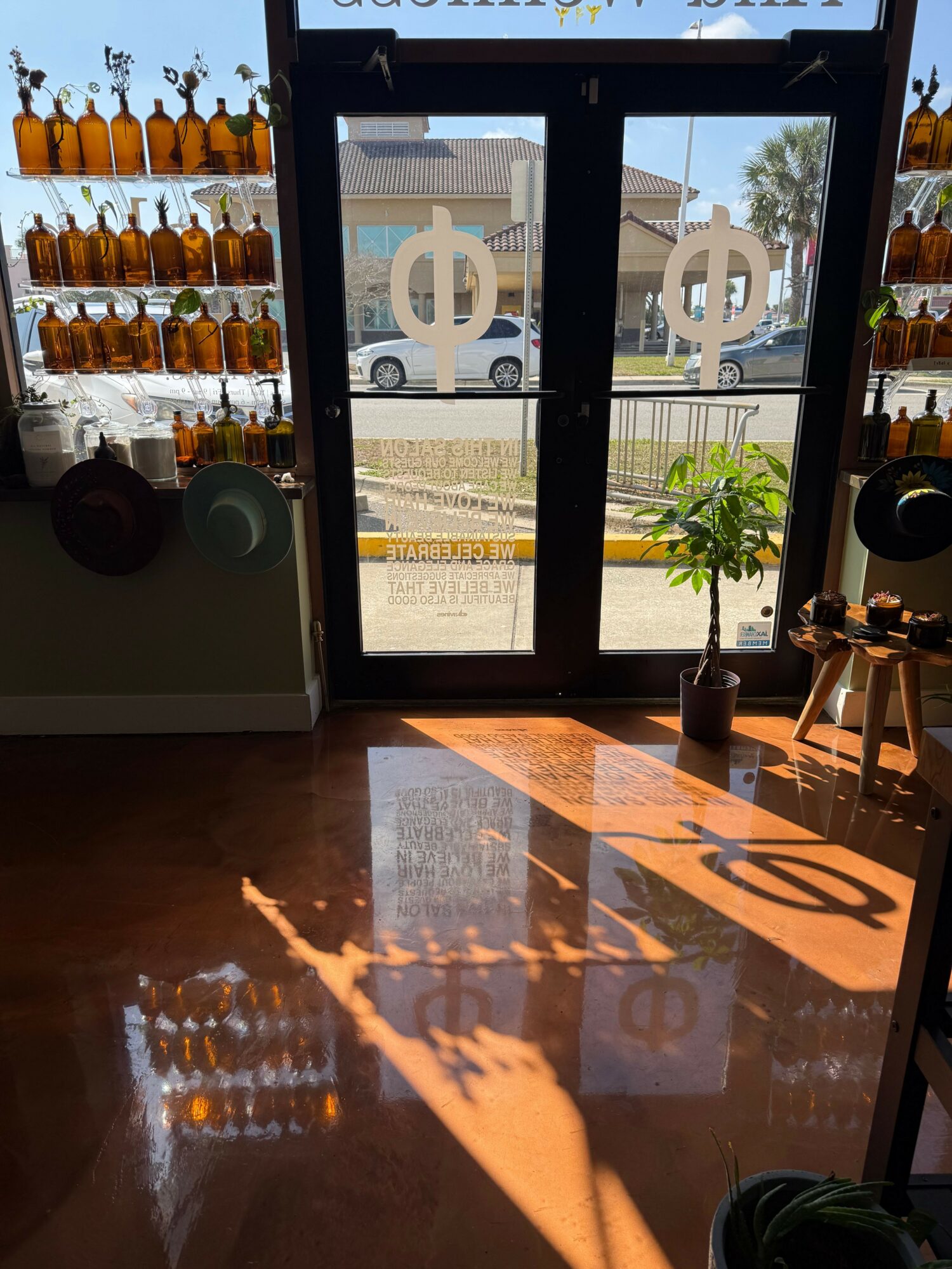 Sunlight casts a shadow of a hand on the floor near a door with symbols, with shelves of bottles on the sides.