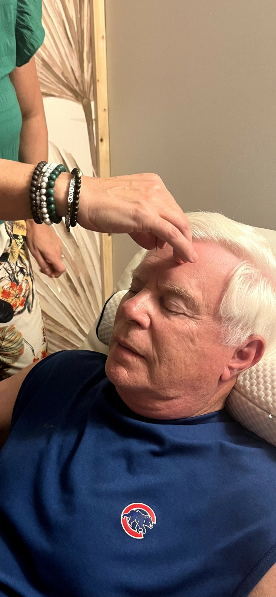 Person applying makeup or skincare to elderly man's forehead indoors.