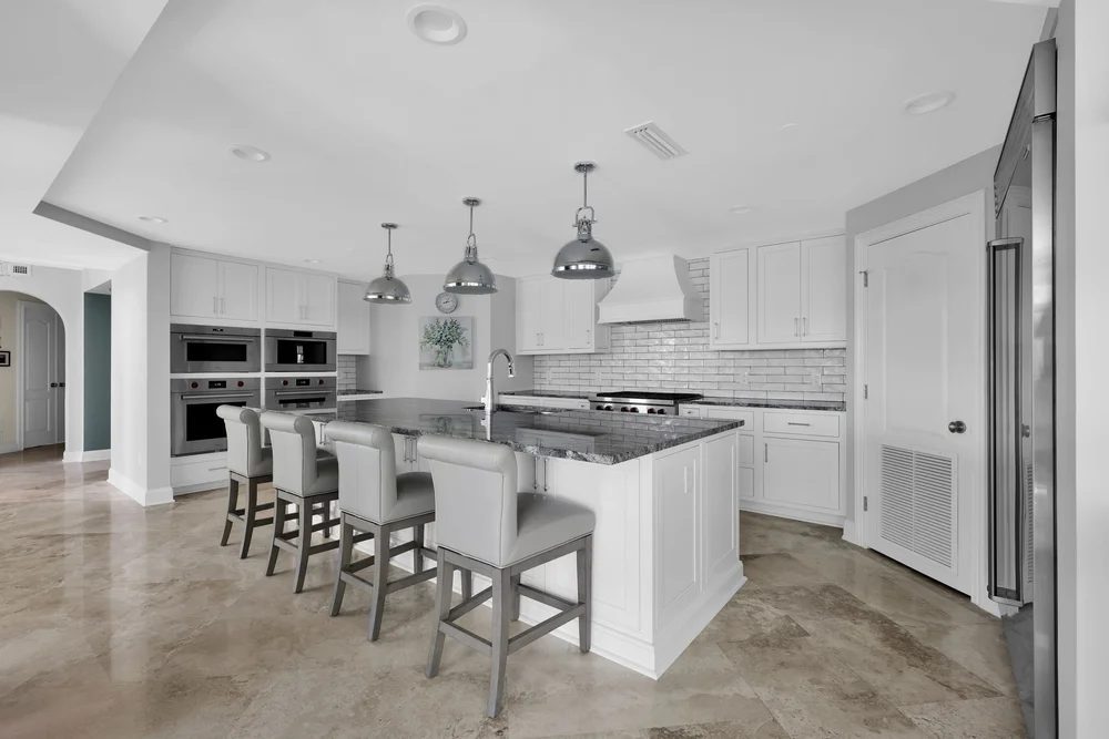 Modern kitchen with white cabinets, island with gray chairs, stainless steel appliances, and pendant lights.