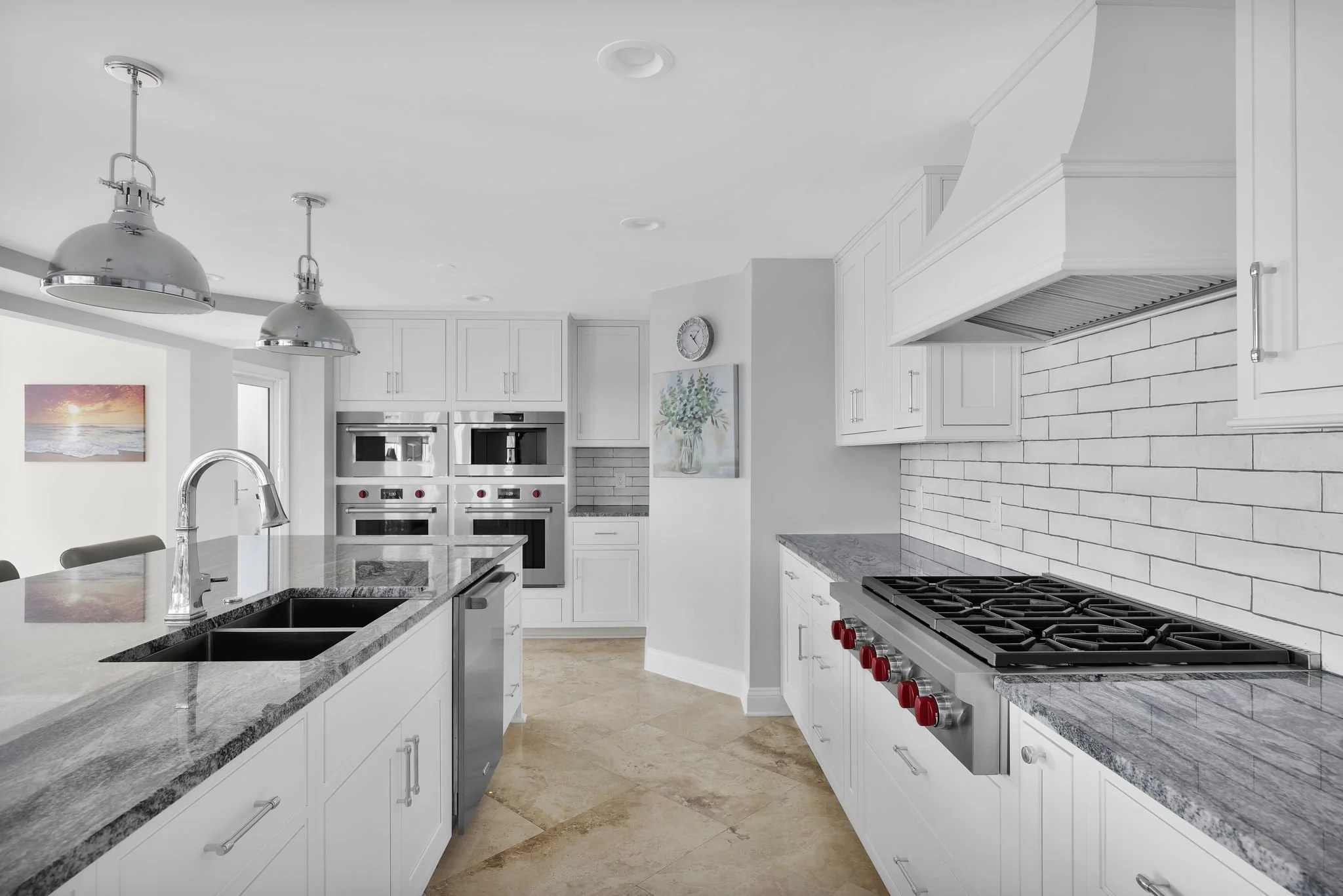 Modern kitchen with white cabinets, stainless steel appliances, a large island with a sink, and a white brick backsplash.