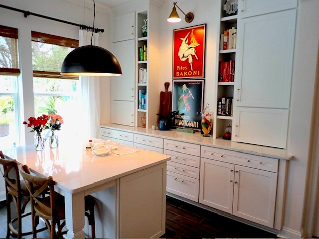 Bright kitchen with white cabinets, a dining table, flowers, and a large window with natural light.