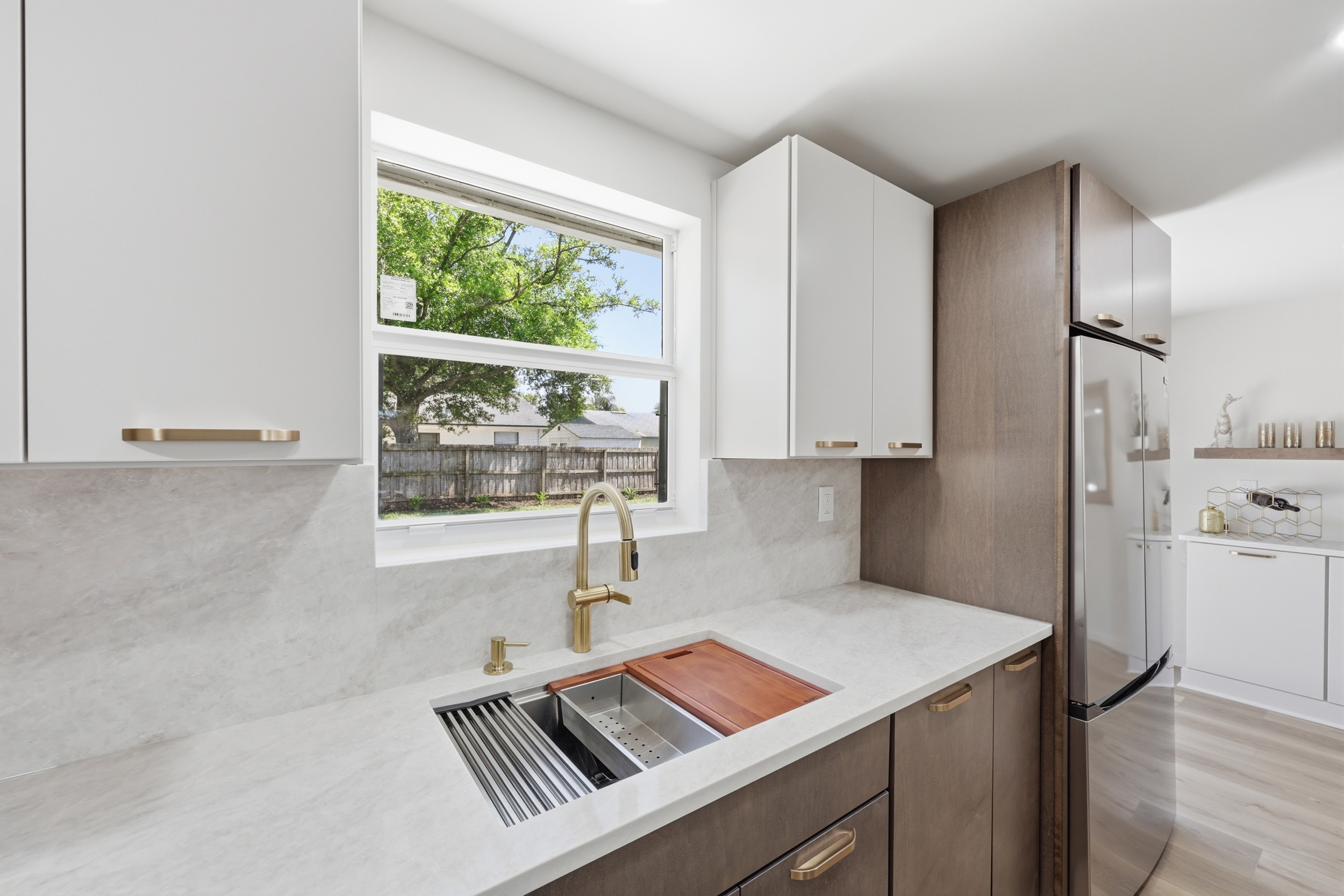 Kitchen with white cabinets, a window, and a sink with a wooden cutting board. Refrigerator and laundry area visible.