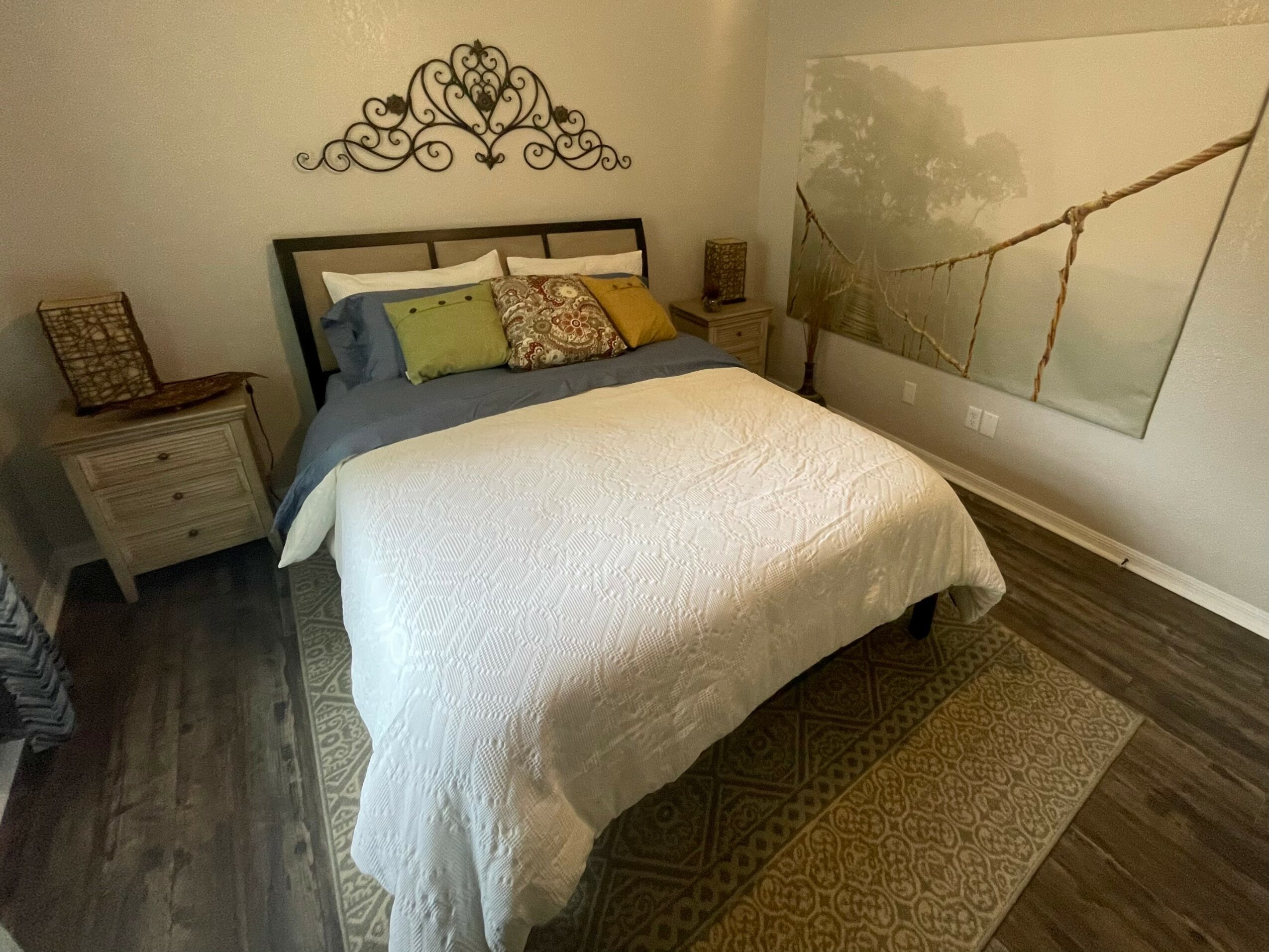 Bedroom with bed, pillows, nightstand, wall art, and hardwood floor.