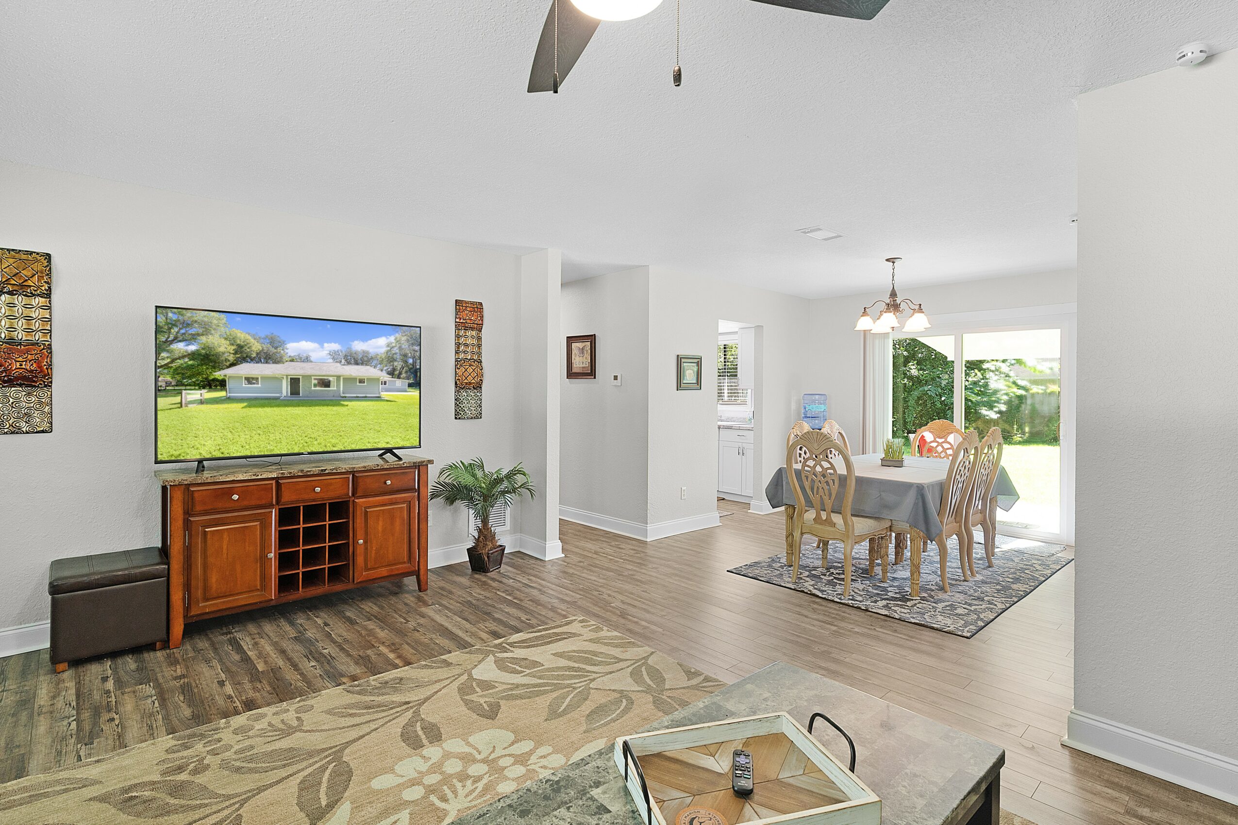 Living room with TV on wooden stand, dining area with table and chairs, and large window with outdoor view.