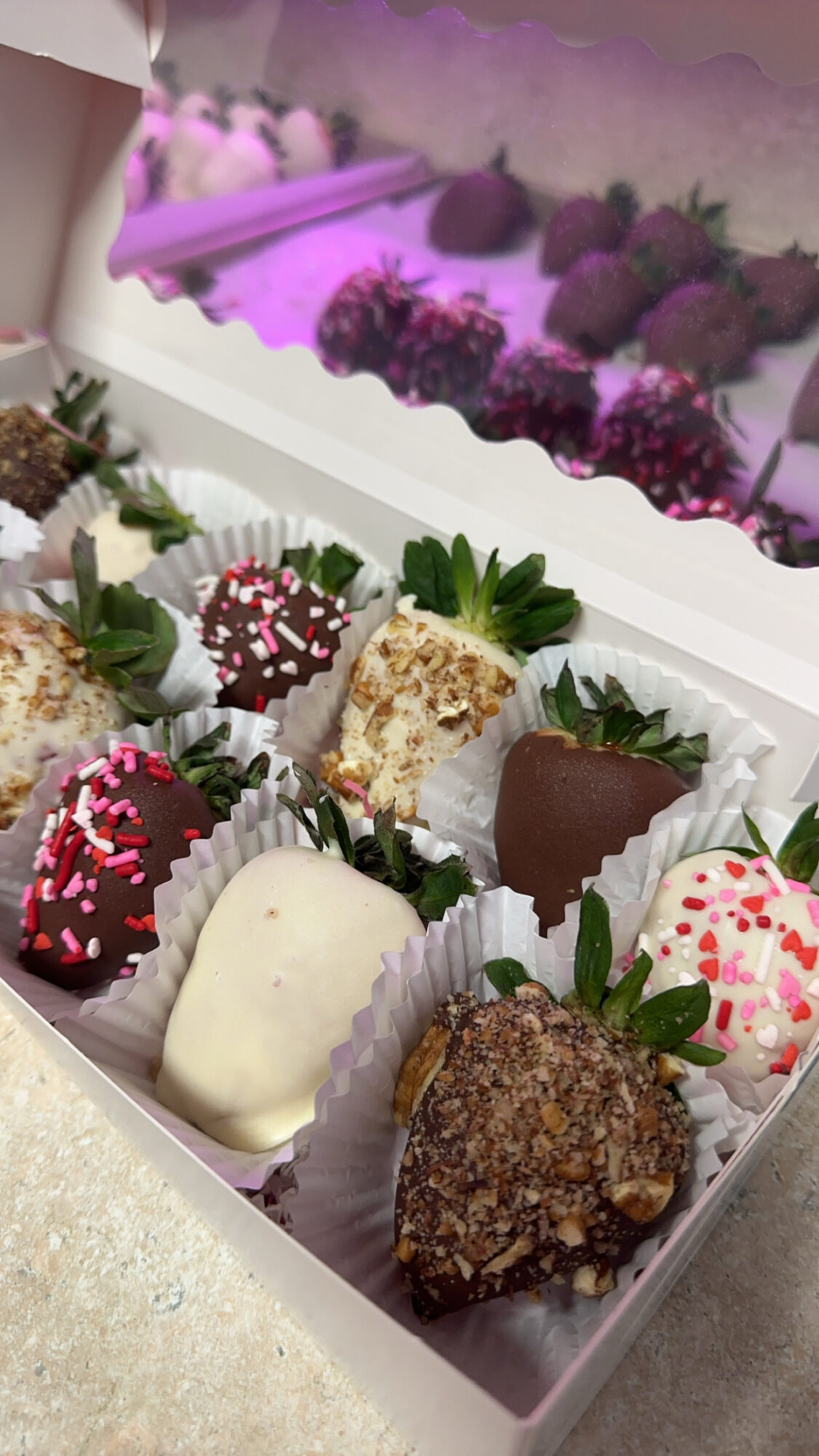 Assorted decorated chocolates and truffles in a box with a purple-lit display in the background.