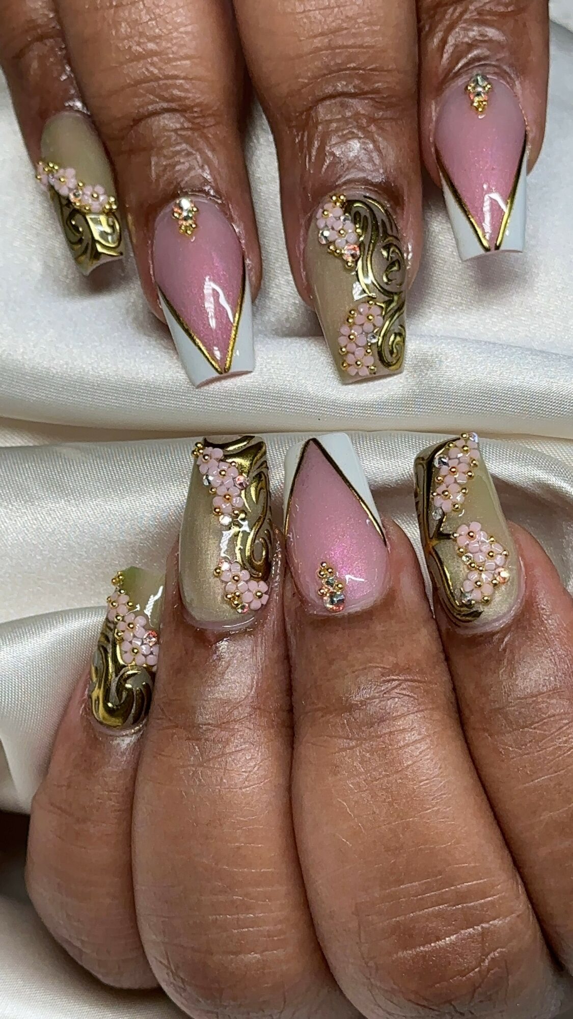 Close-up of manicured nails with pink, gold, and floral designs, some with rhinestones and gold accents.