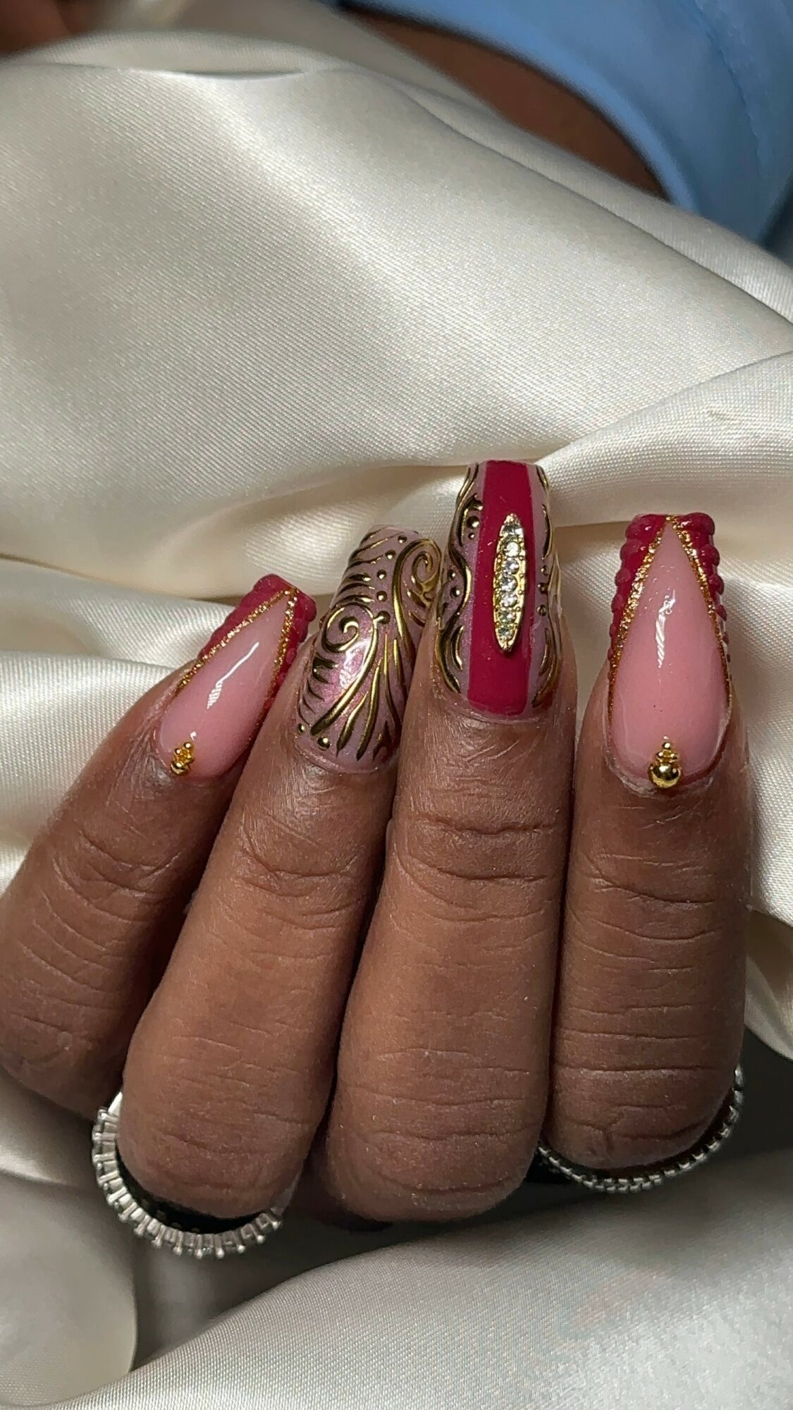Close-up of four fingers with decorated nails resting on white satin fabric.