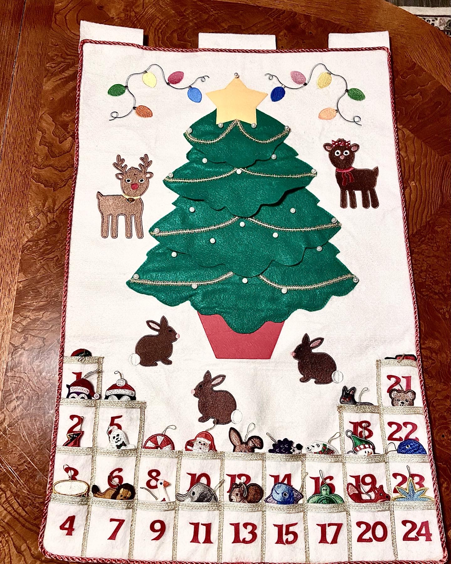 Decorative Christmas-themed fabric with a Christmas tree, reindeer, rabbits, and numbered blocks, on a wooden surface.
