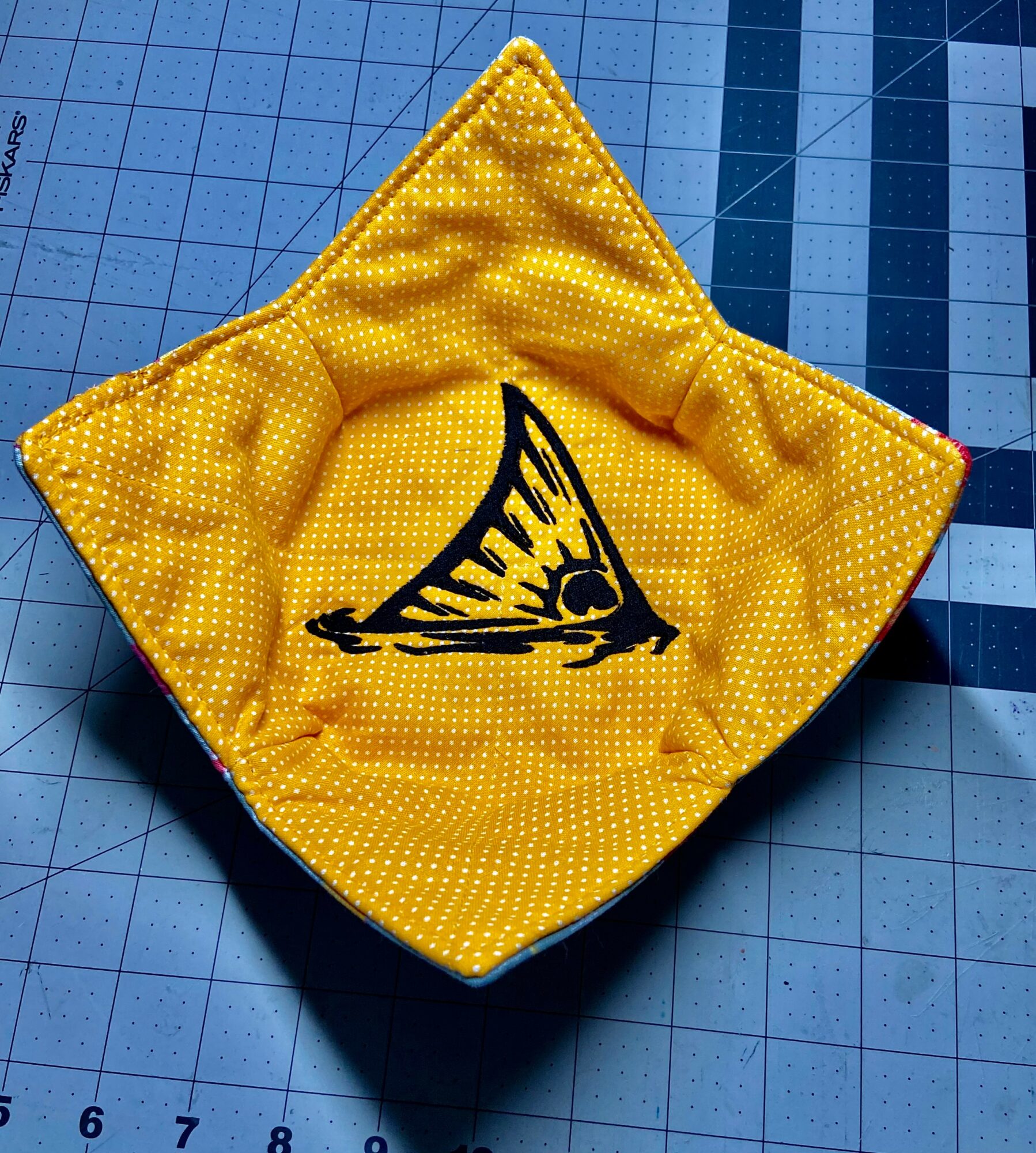 Open yellow fabric pouch with black butterfly wing design inside, on a blue cutting mat.