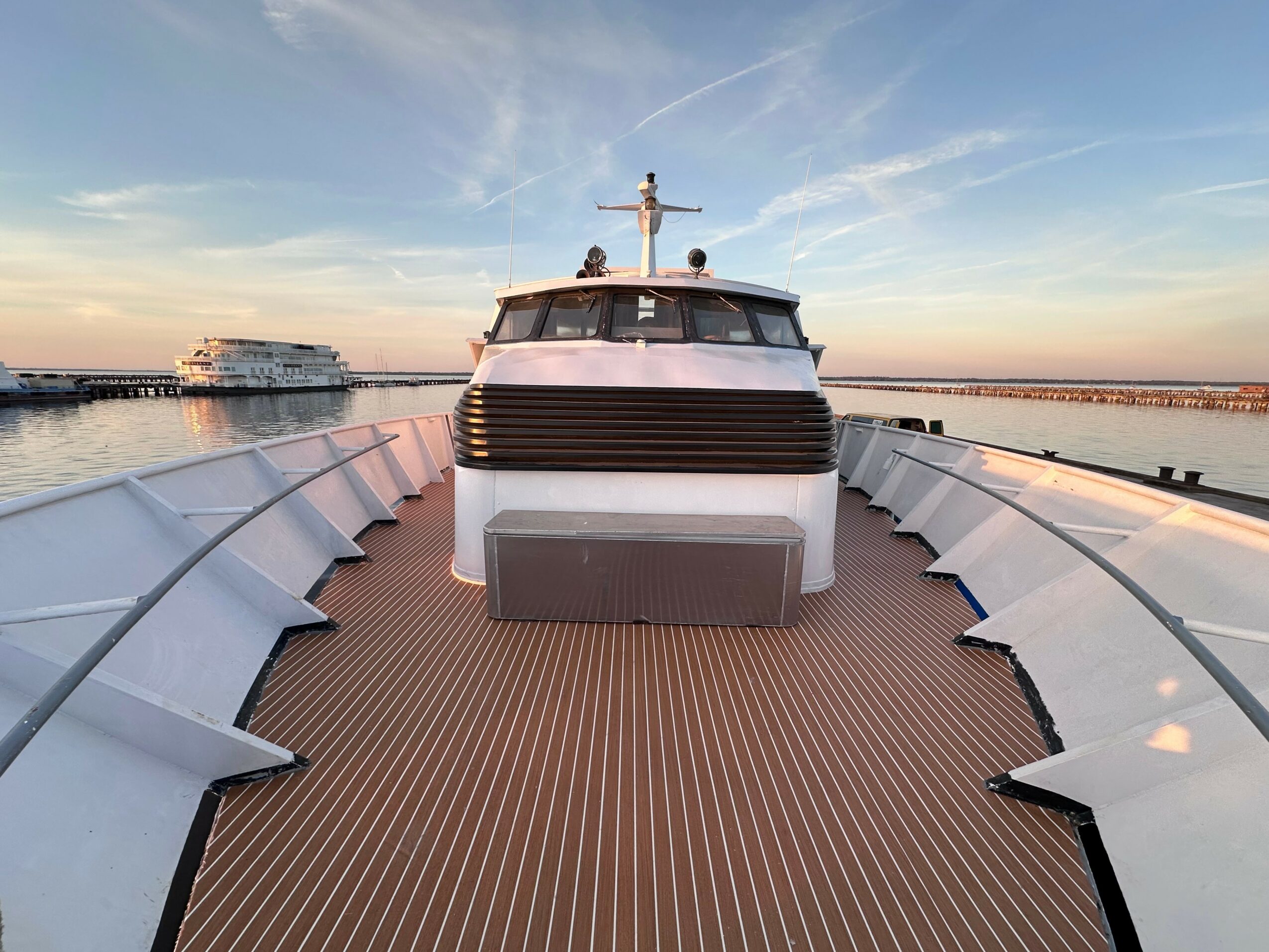 View from the front of a yacht on water during sunset, with another boat in the background, and a clear sky.