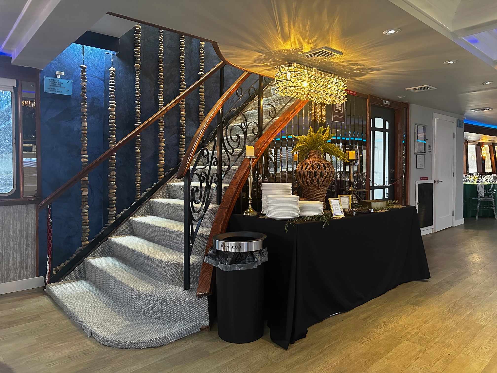 Elegant staircase with a decorative railing, chandelier, and a table with white items and flowers nearby.