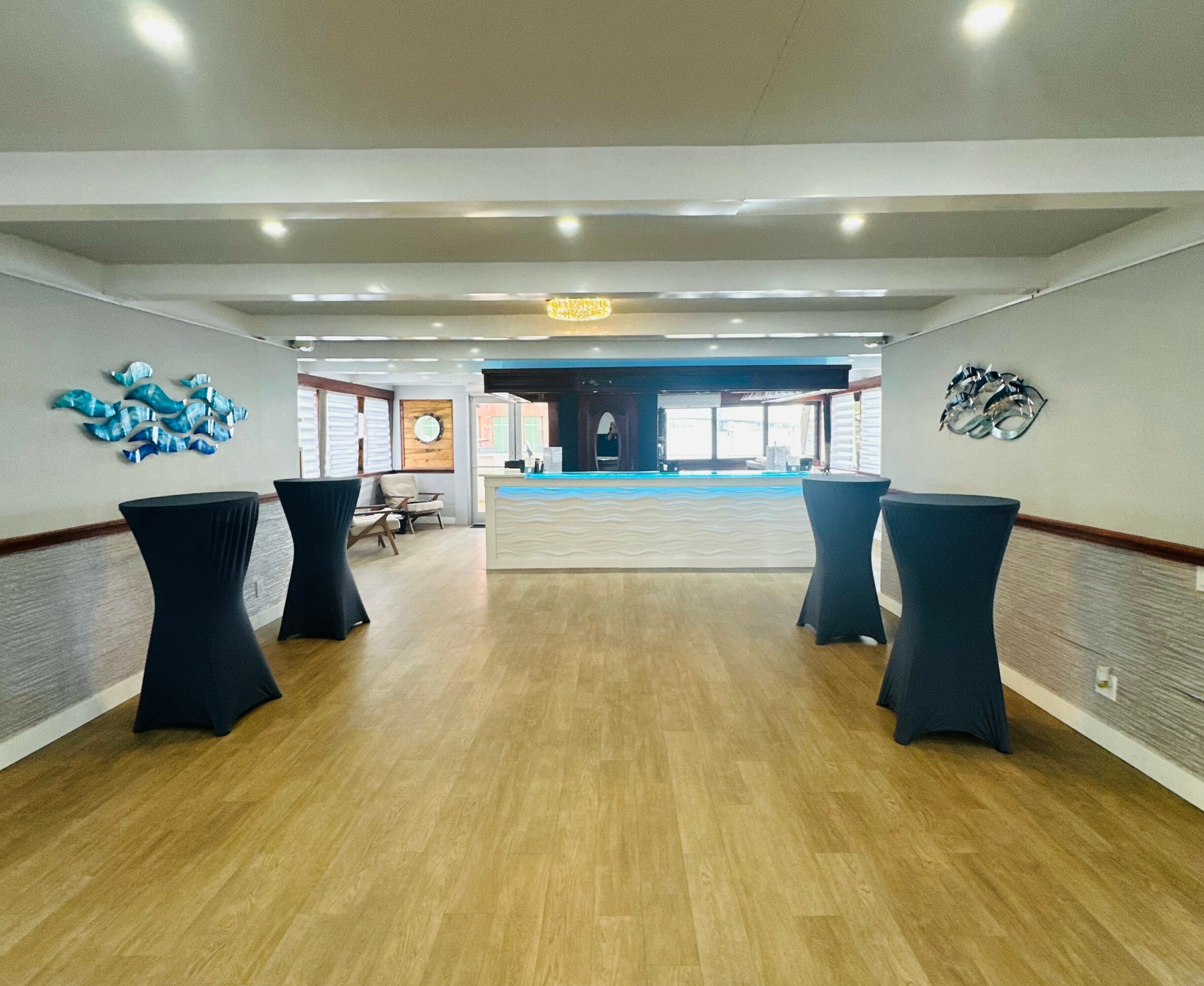 Empty room with four tall cocktail tables covered with black cloths, artwork on walls, and a bar area in the background.
