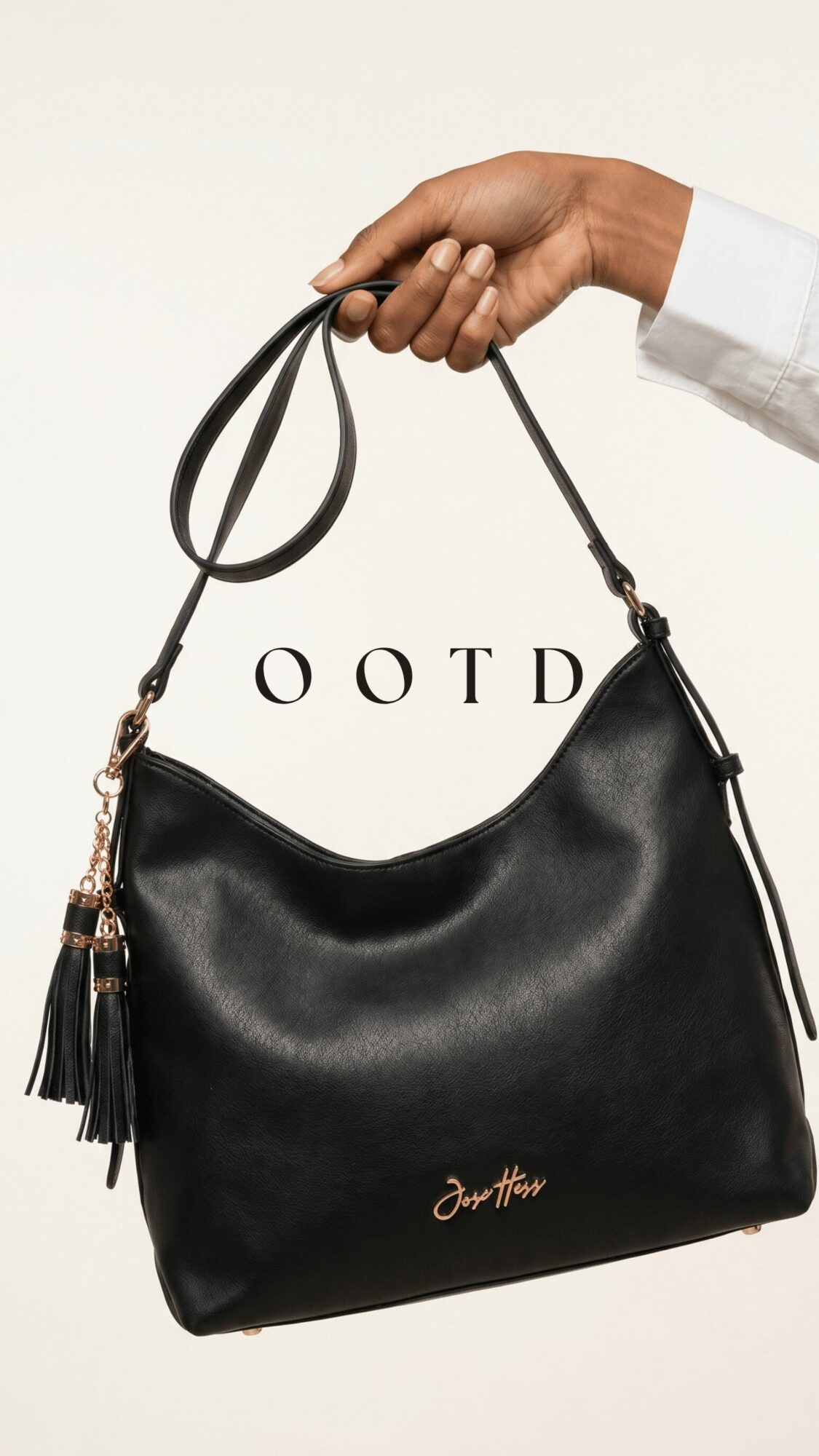 Hand holding a black handbag with a tassel and gold logo, against a plain background.
