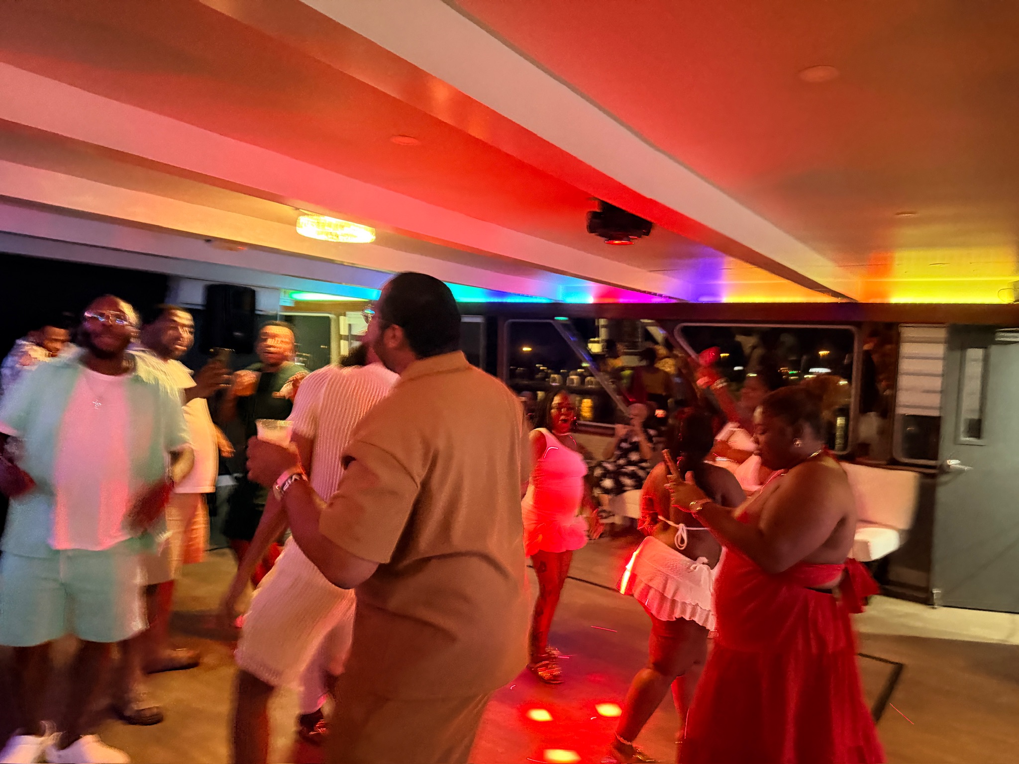 People dancing and socializing in a colorful indoor party setting with vibrant lighting.