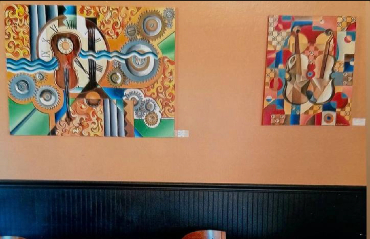 Two colorful abstract paintings on a beige wall above a dark blue wainscot, with a small part of a table visible.