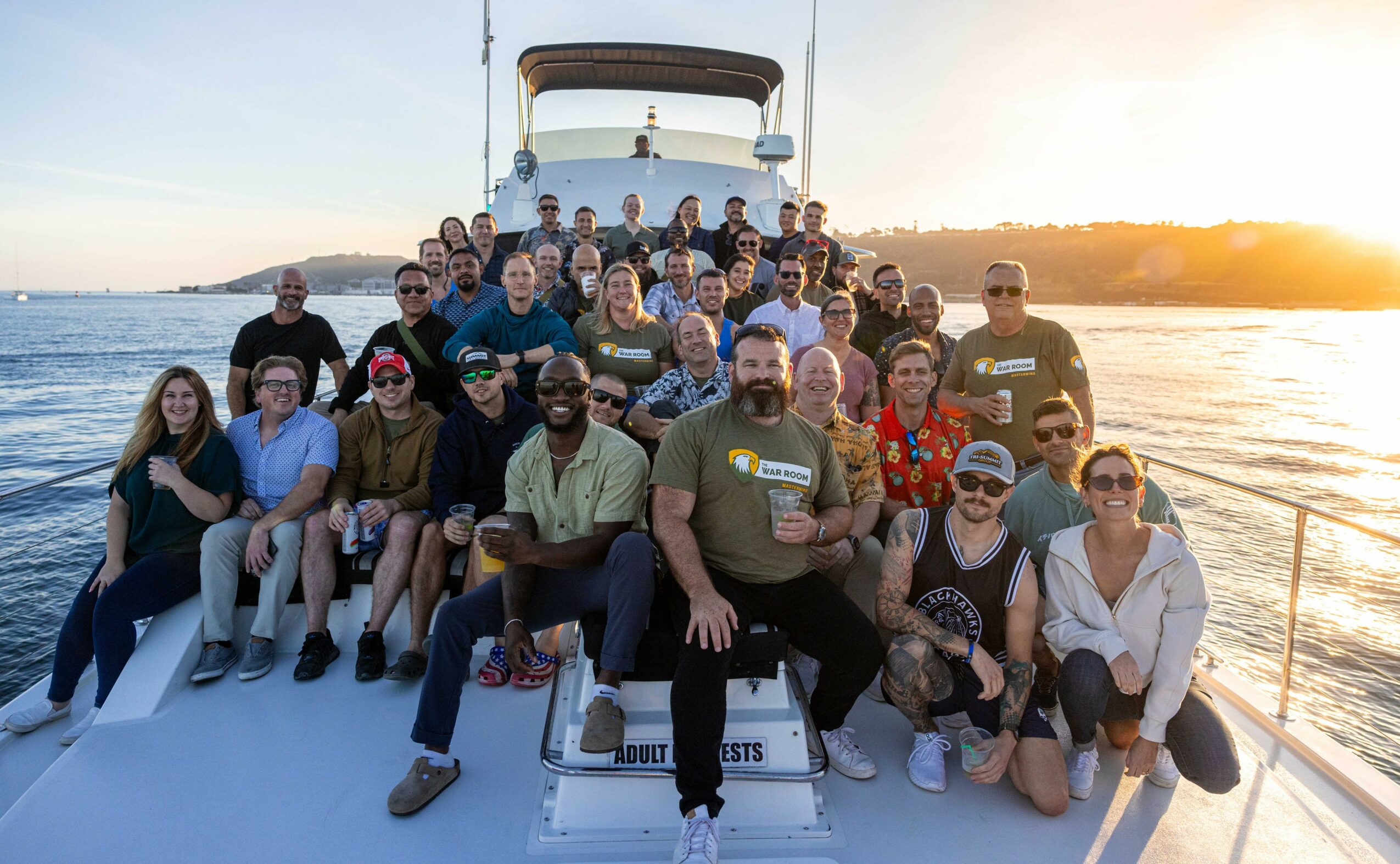 Group of people on a boat during sunset, smiling and posing for a photo, with water and sky in the background.