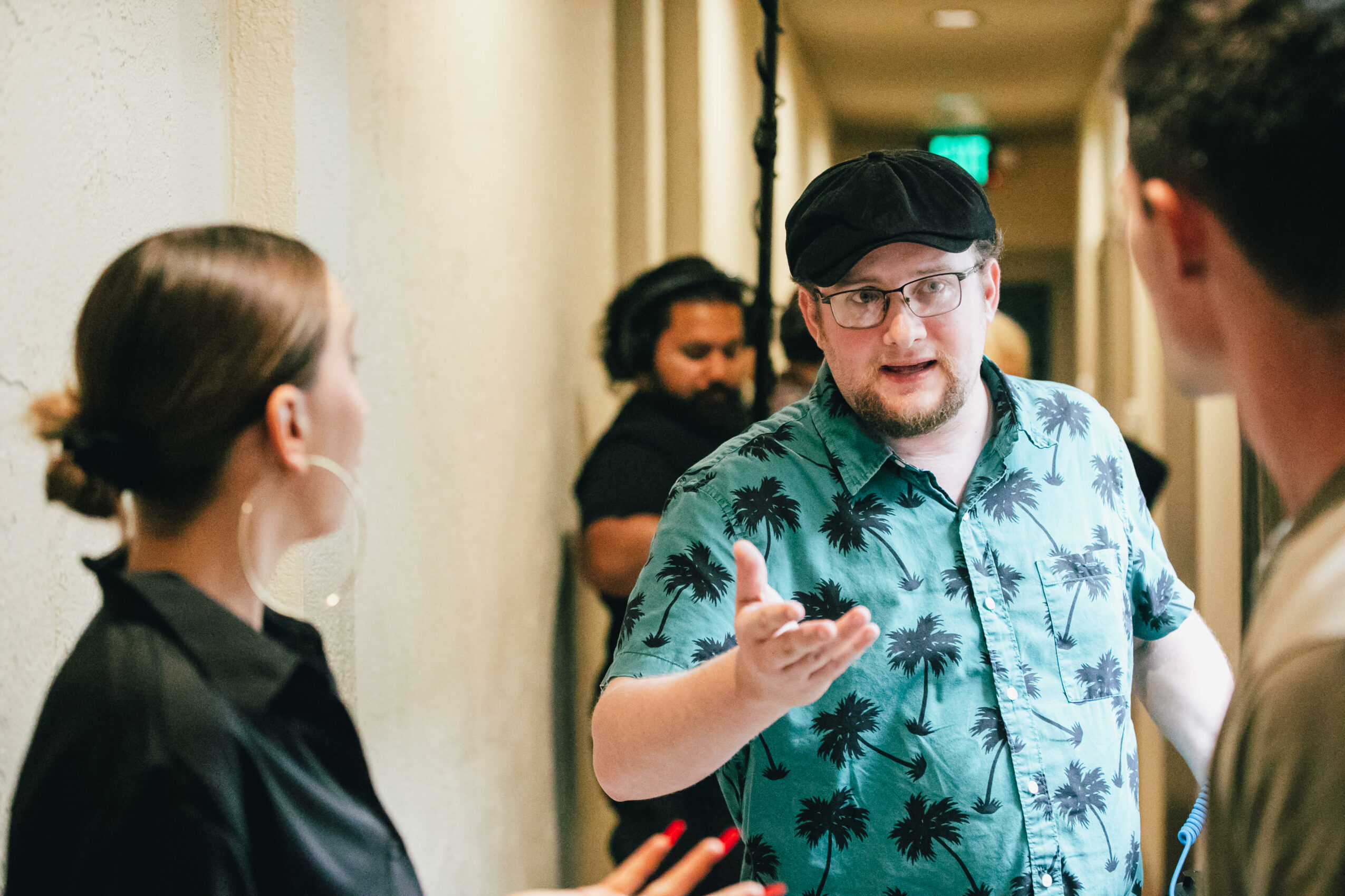 Group of people engaged in conversation indoors, with a man in a tropical shirt gesturing as he speaks.