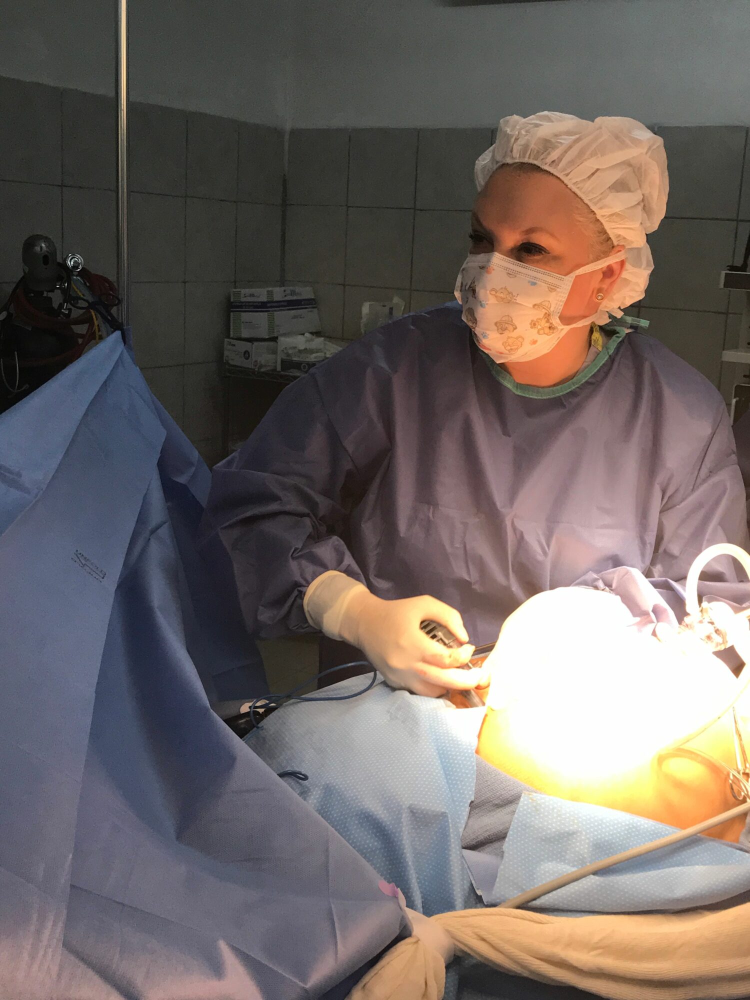 Surgeon in scrubs and mask performing surgery in an operating room, illuminated by bright surgical light.