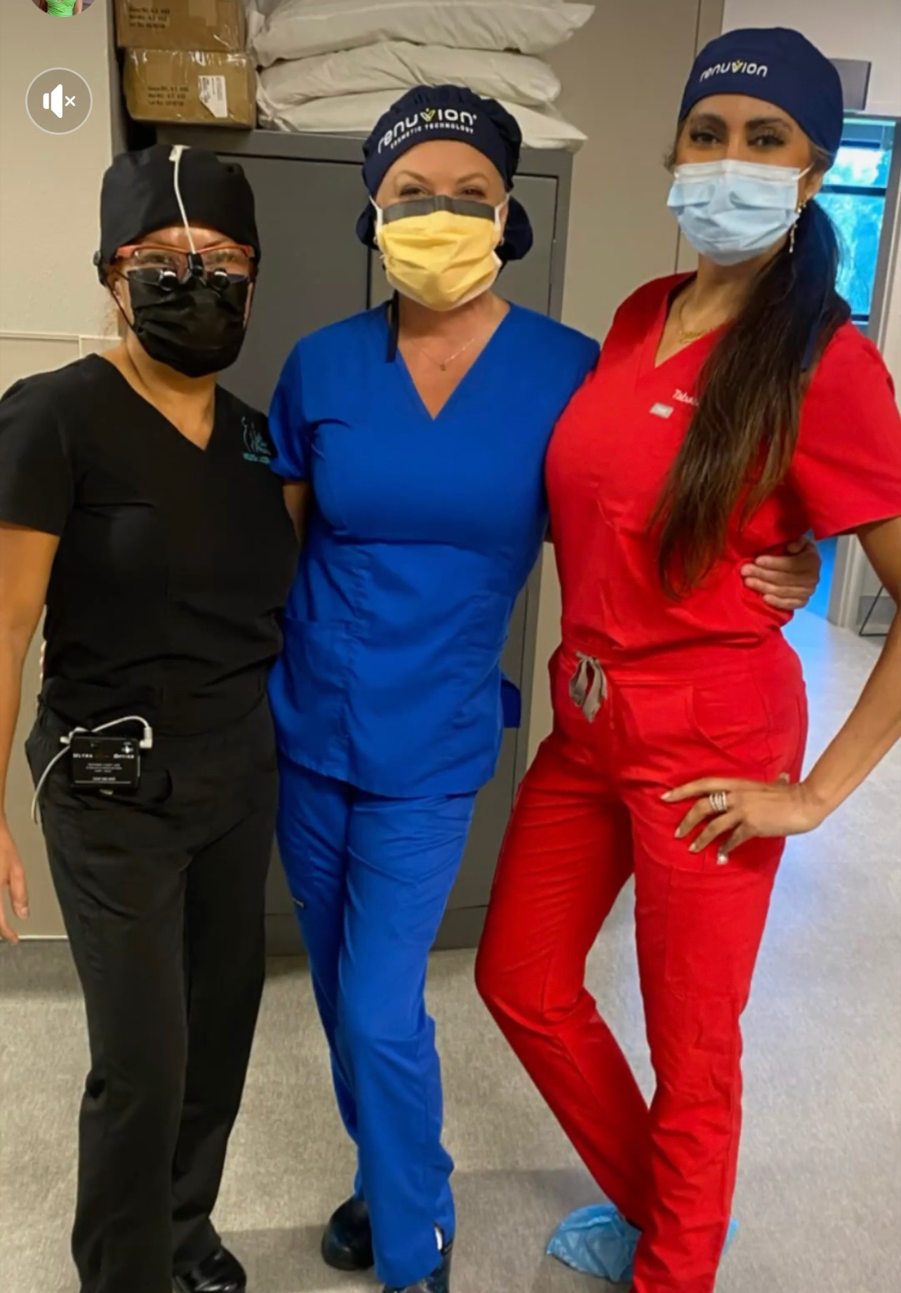 Three healthcare workers in scrubs and masks standing together in a clinical setting.