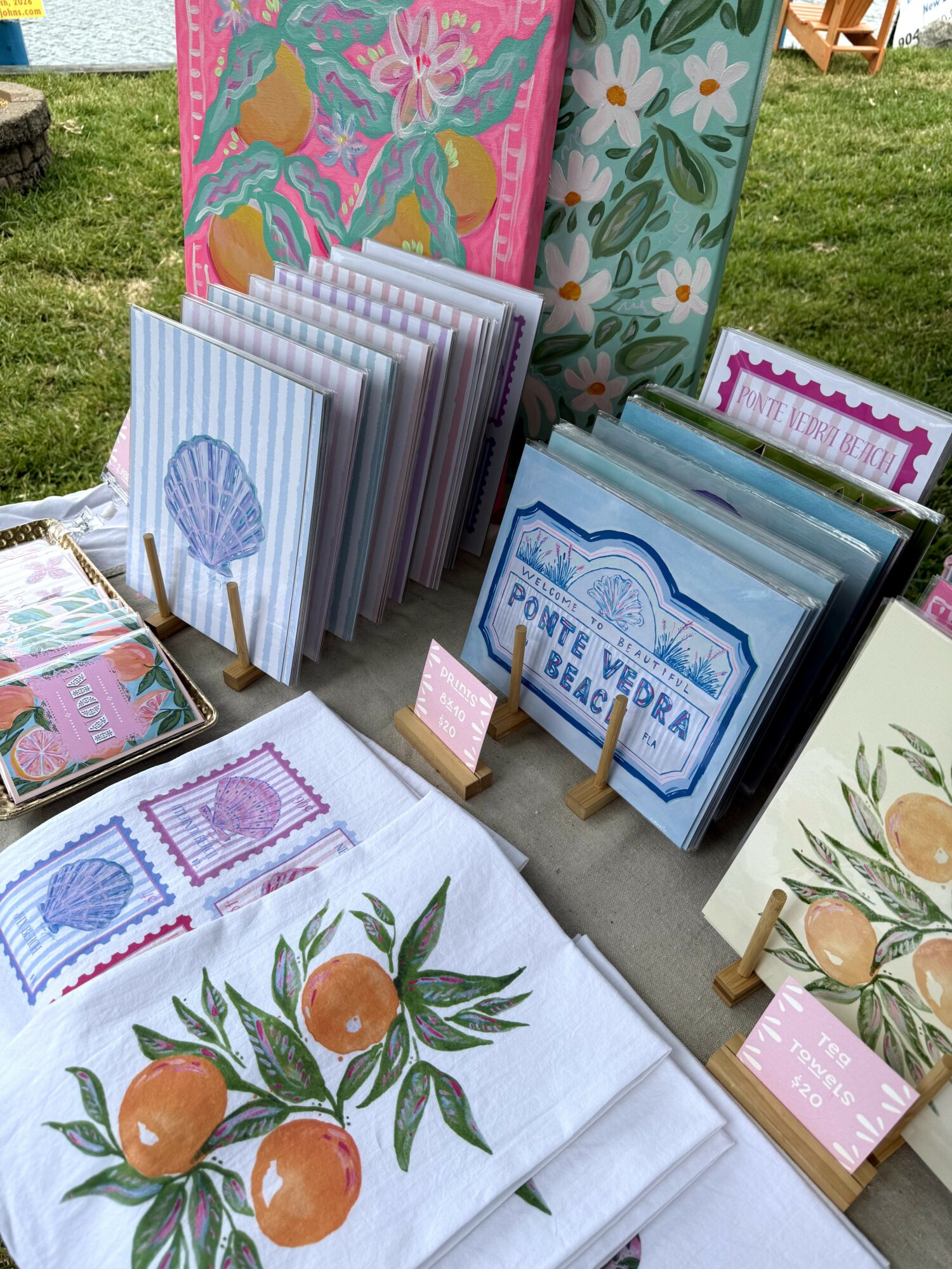 Display of colorful illustrated books and fabric with fruit and floral designs on a table outdoors.