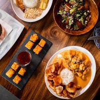 Assorted dishes on a wooden table, including sushi, salad, and a curry with rice, viewed from above.